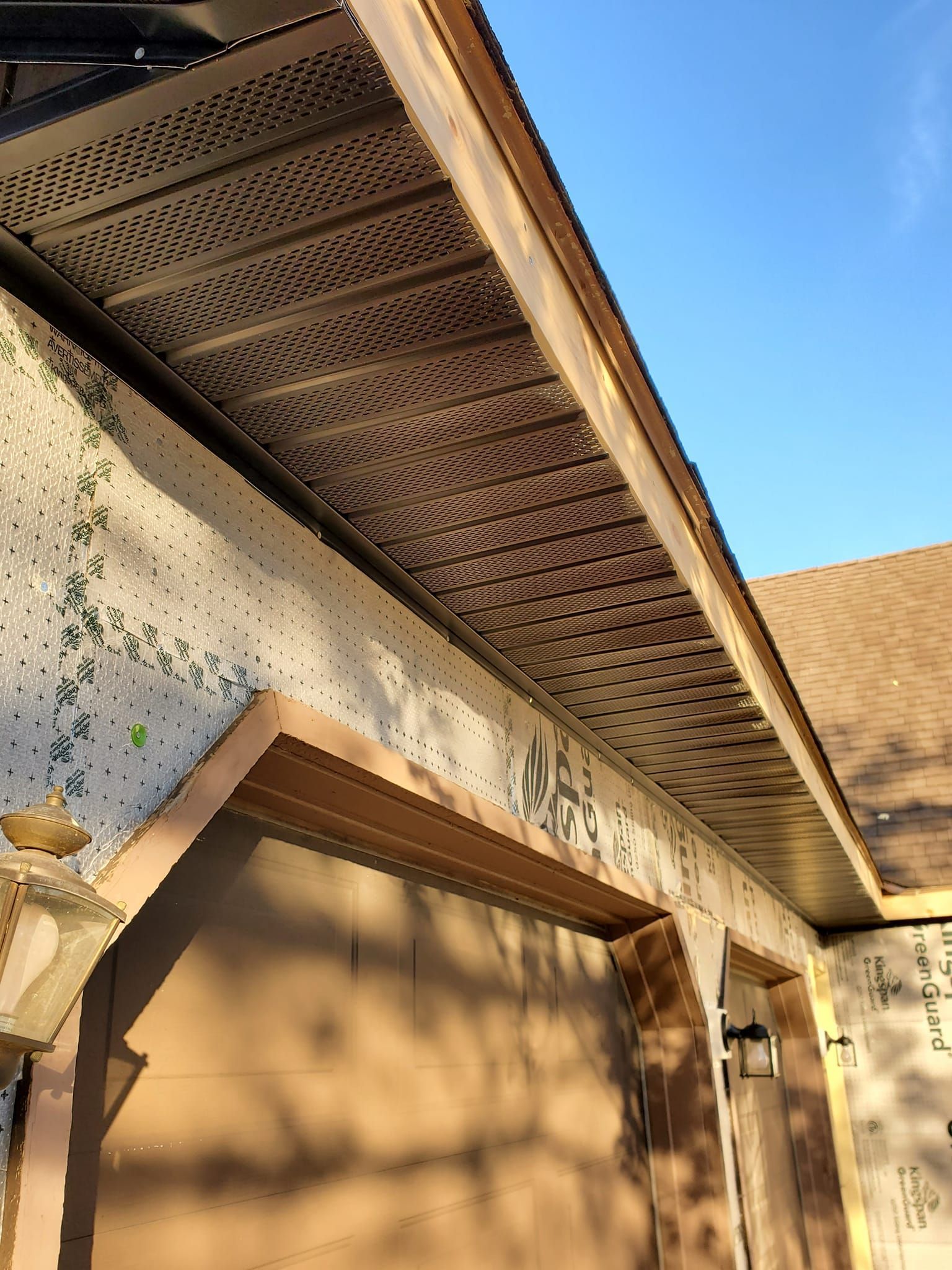 Sunlit exterior of a stucco building with a decorative perforated roof overhang and blue sky above