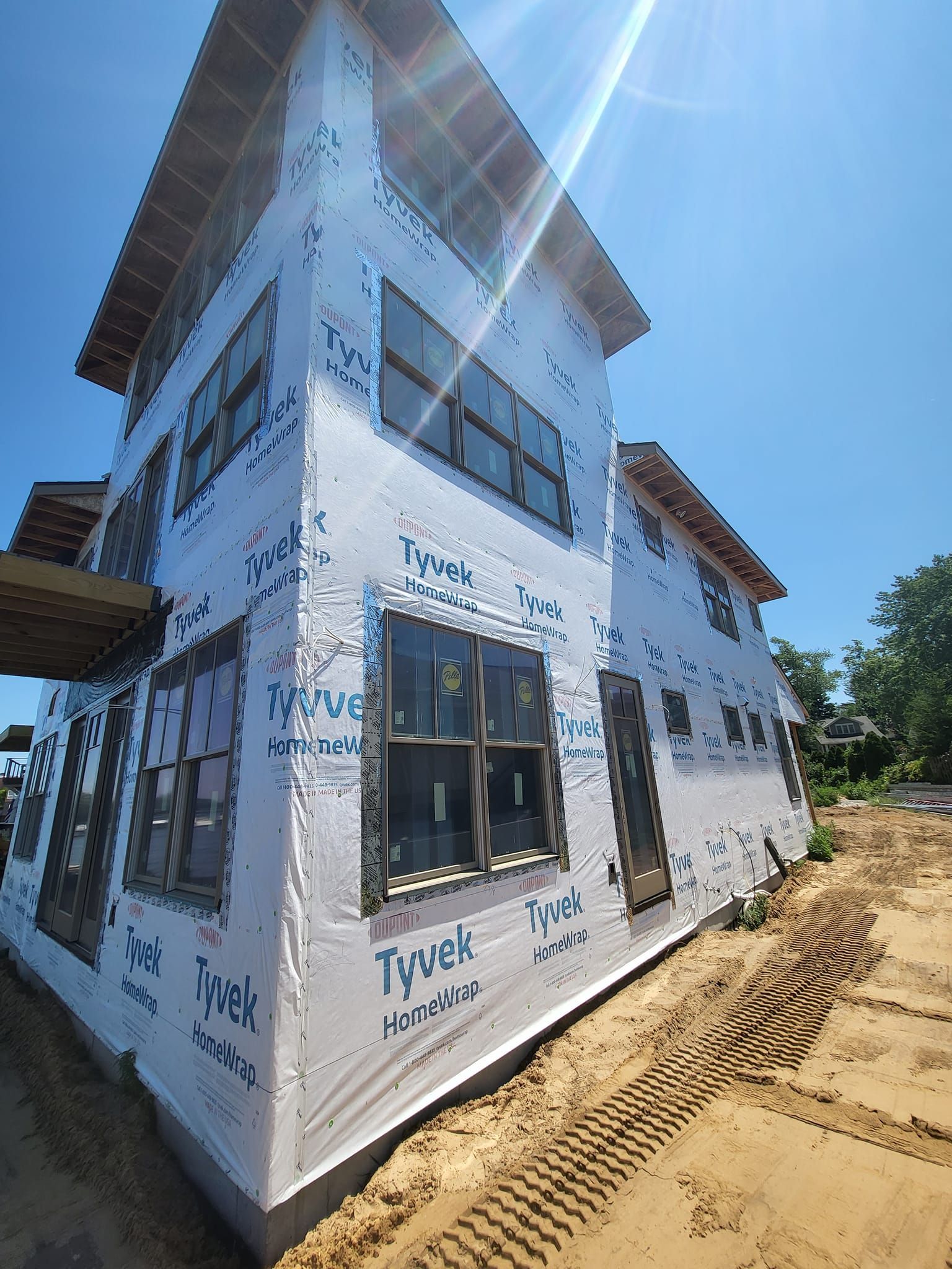 Partially built white house wrapped in house wrap, viewed from the corner under a blue sky