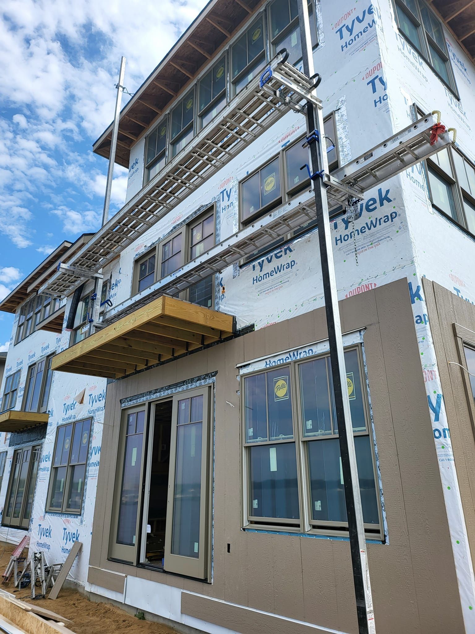 Two-story house exterior with beige siding, white trim, balconies, and large windows under a blue sky