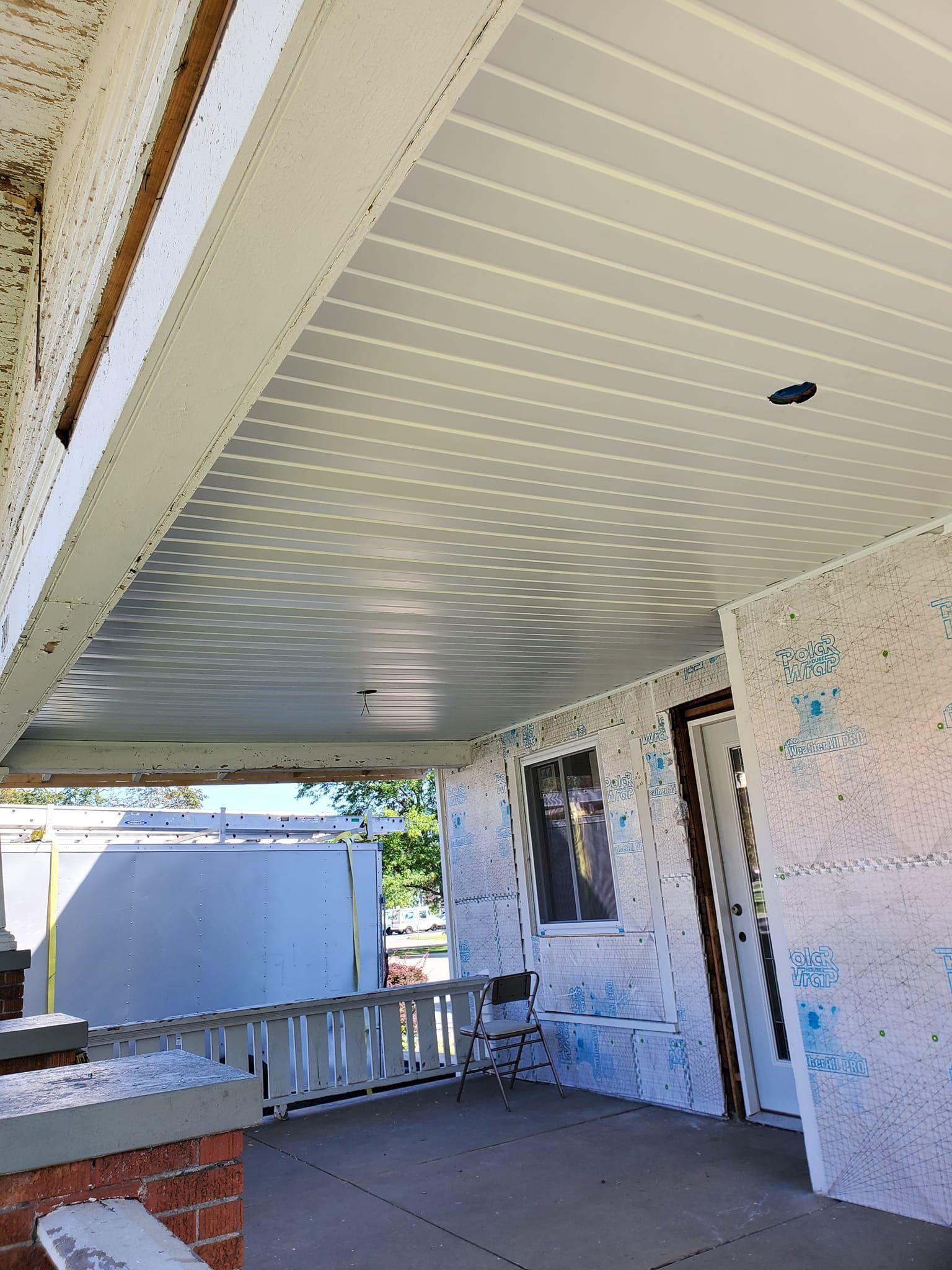 Covered porch with white beadboard ceiling, brick ledge, and exterior walls in renovation work