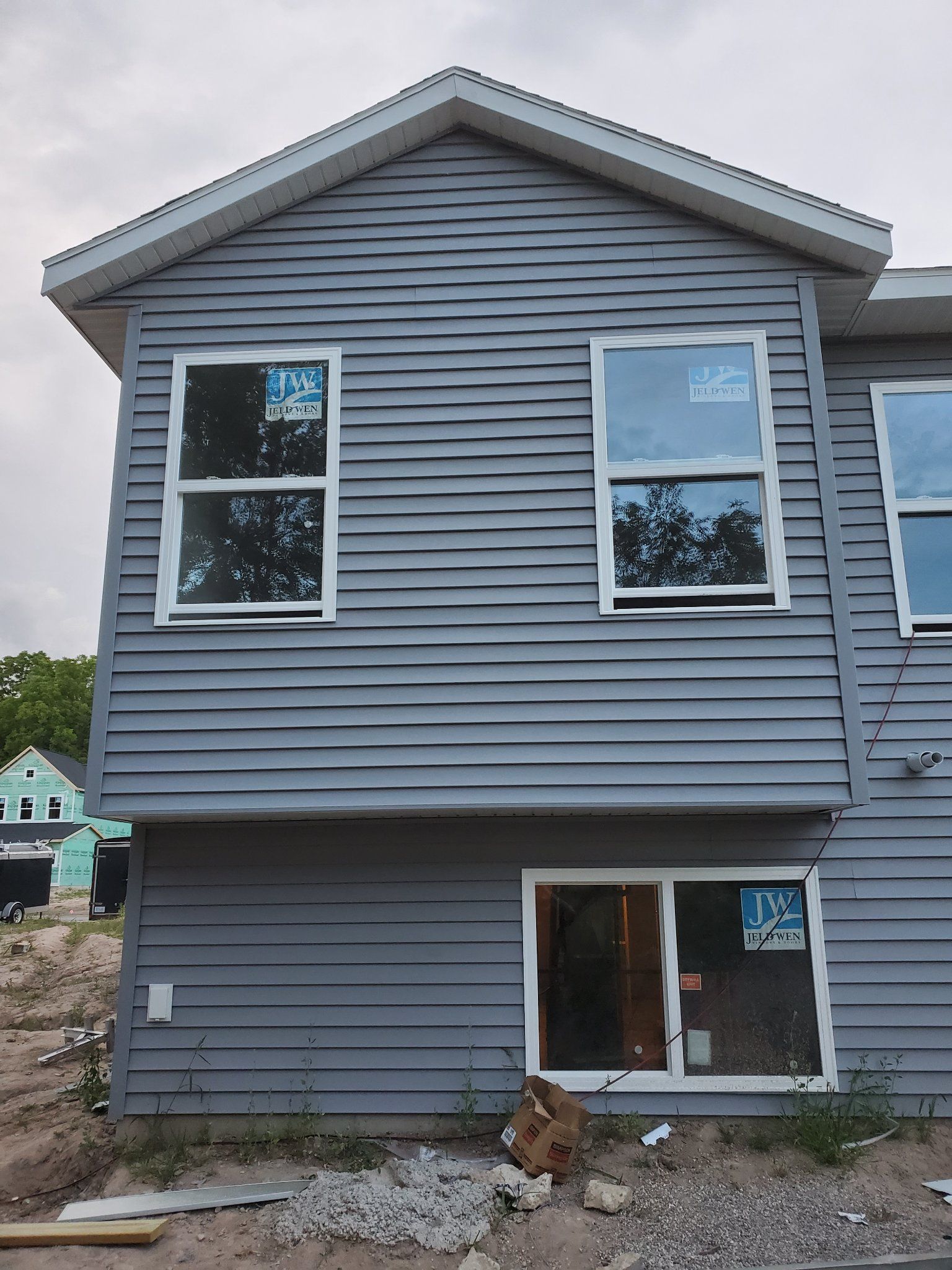 Gray two-story house with horizontal siding, two upper windows, and a small lower entrance window.