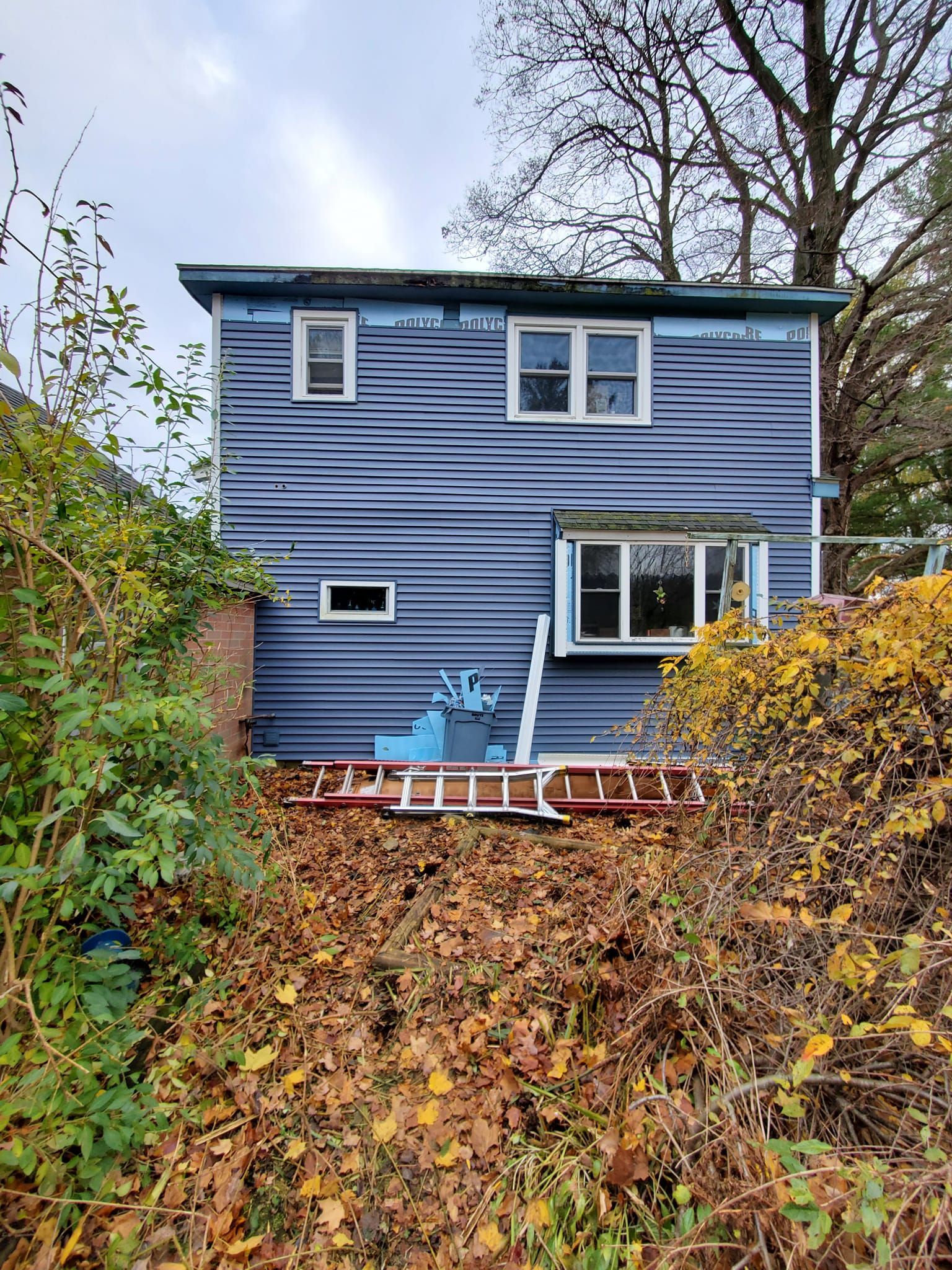 Blue two-story house with deck and autumn foliage on a steep hillside