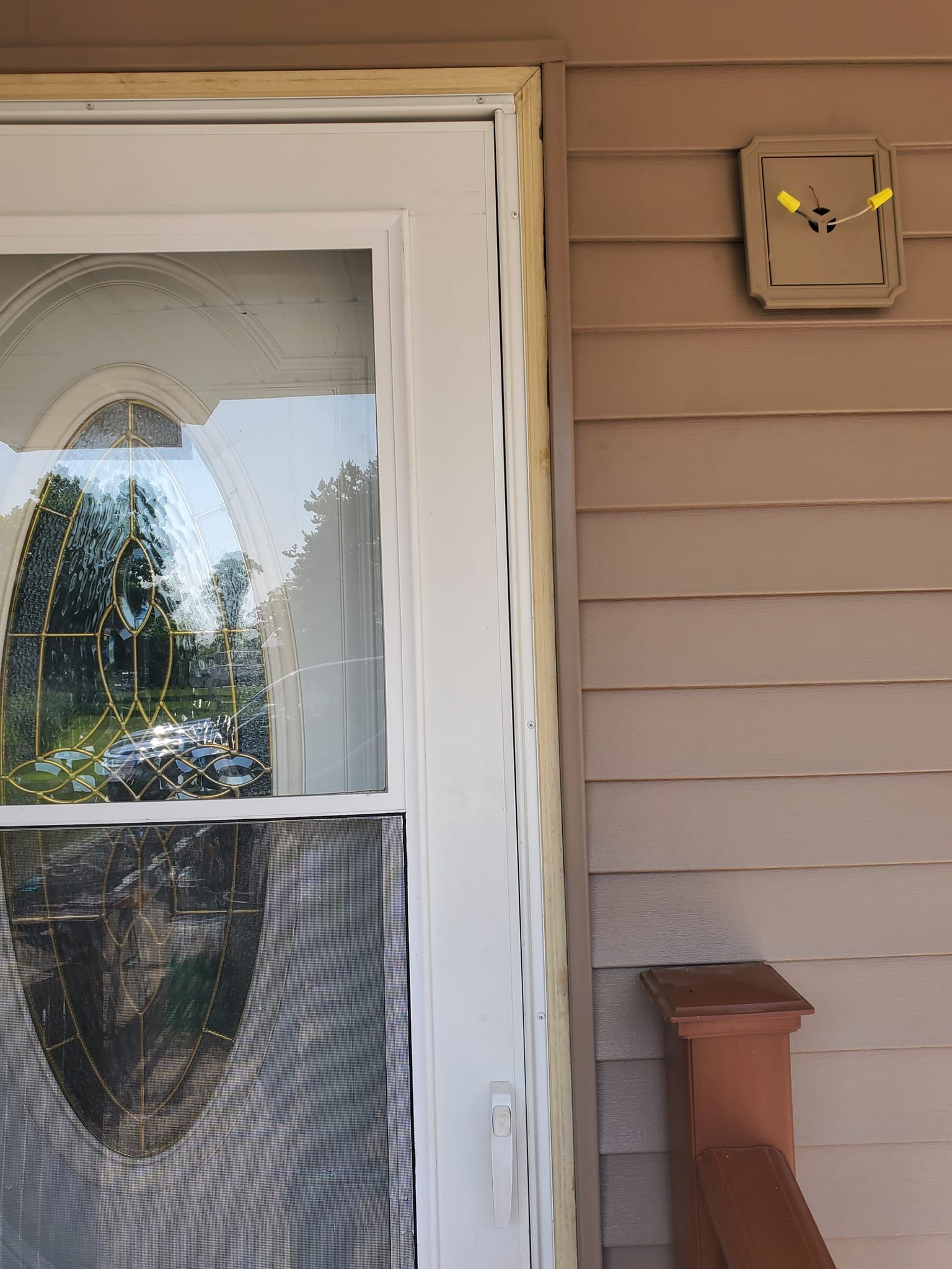Front porch door with white trim, oval glass window, and beige siding with a utility box nearby