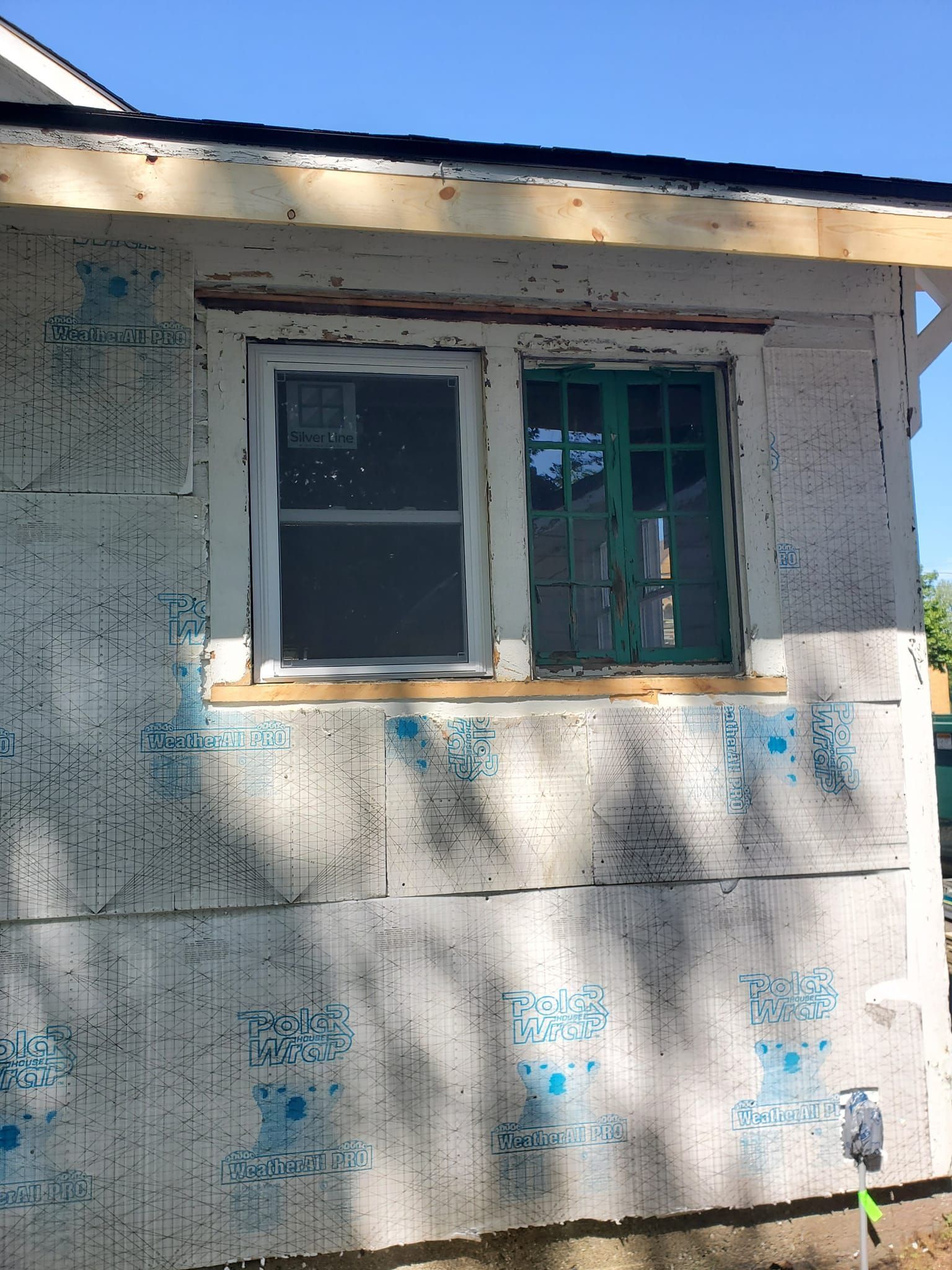 Weathered white house wall with a small window and peeling blue paint in sunlight and shadow.