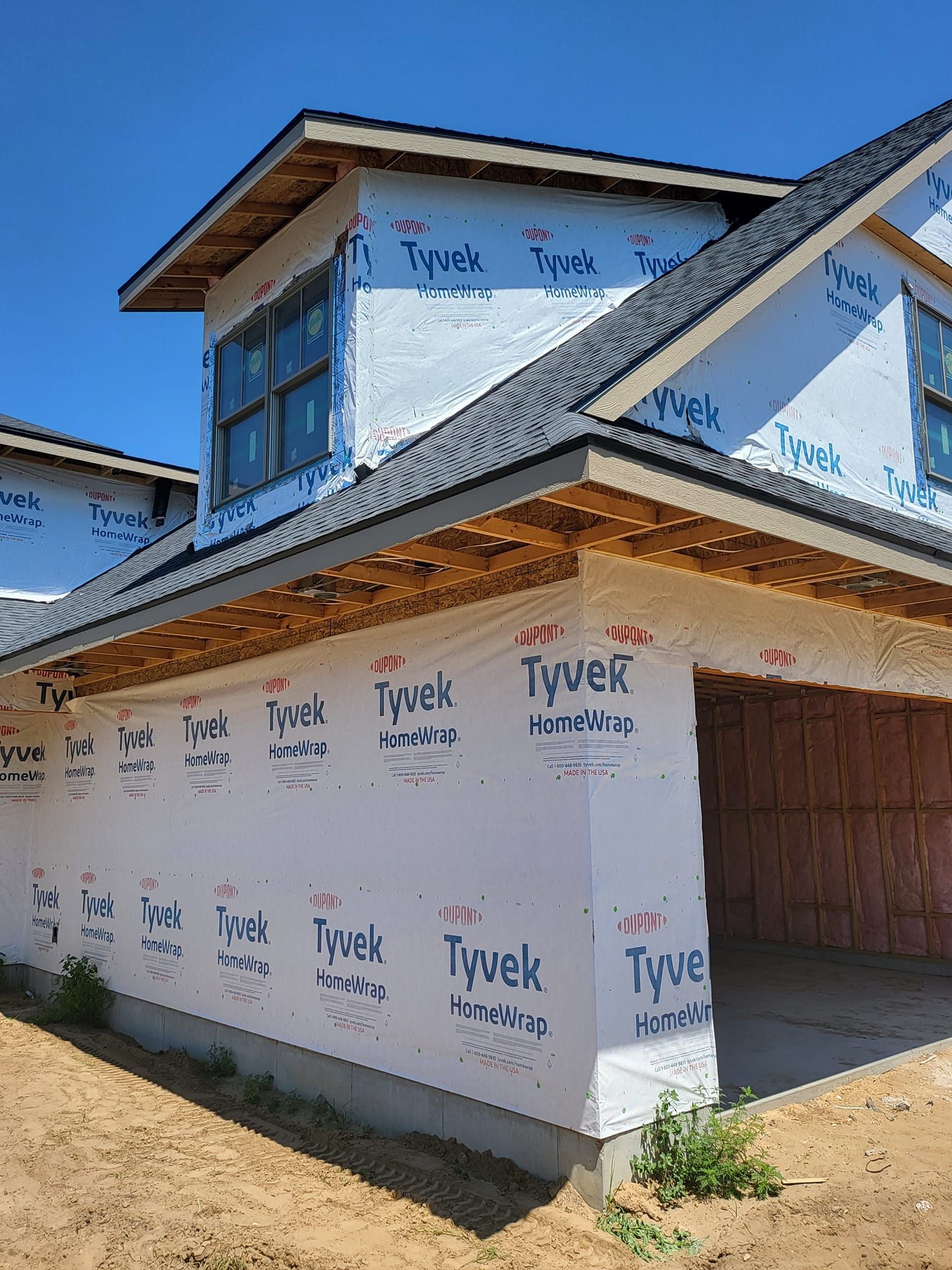 Partially built house wrapped in Tyvek house wrap under a blue sky