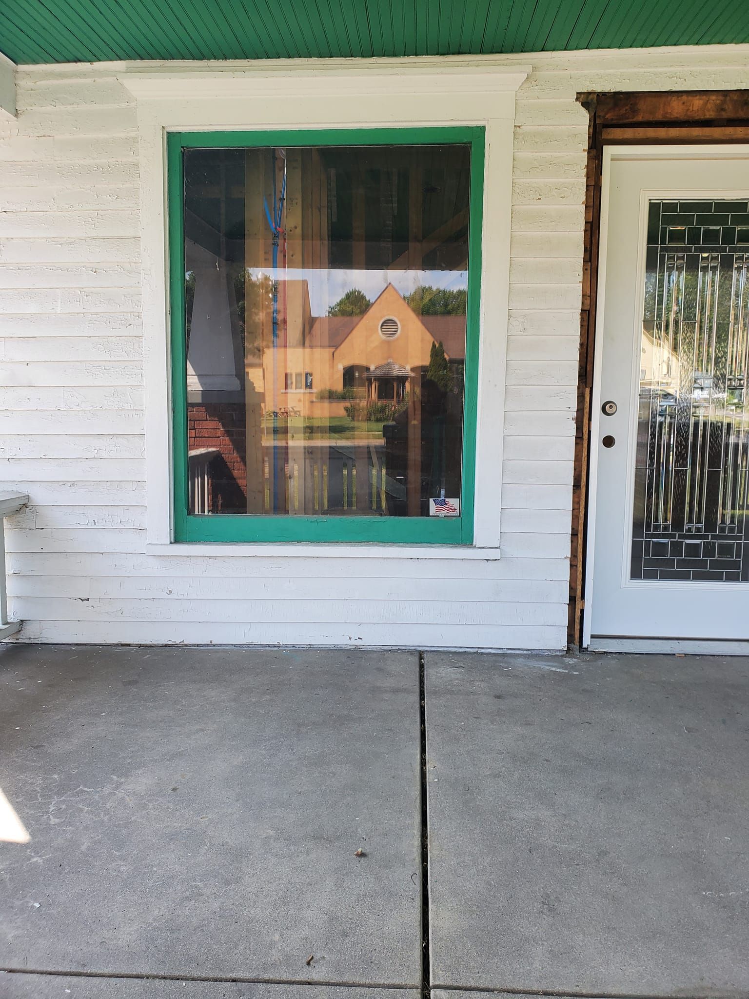 Front porch with green-trimmed window, white siding, and a glass front door.