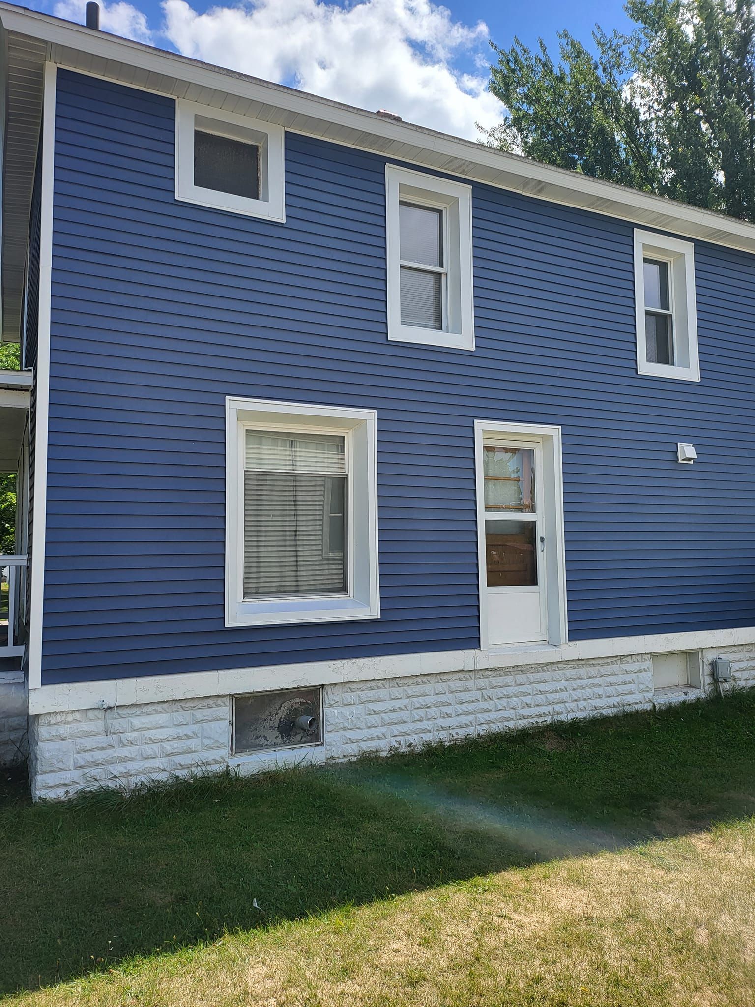 Blue two-story house with white trim, a white door, and a small lawn in front