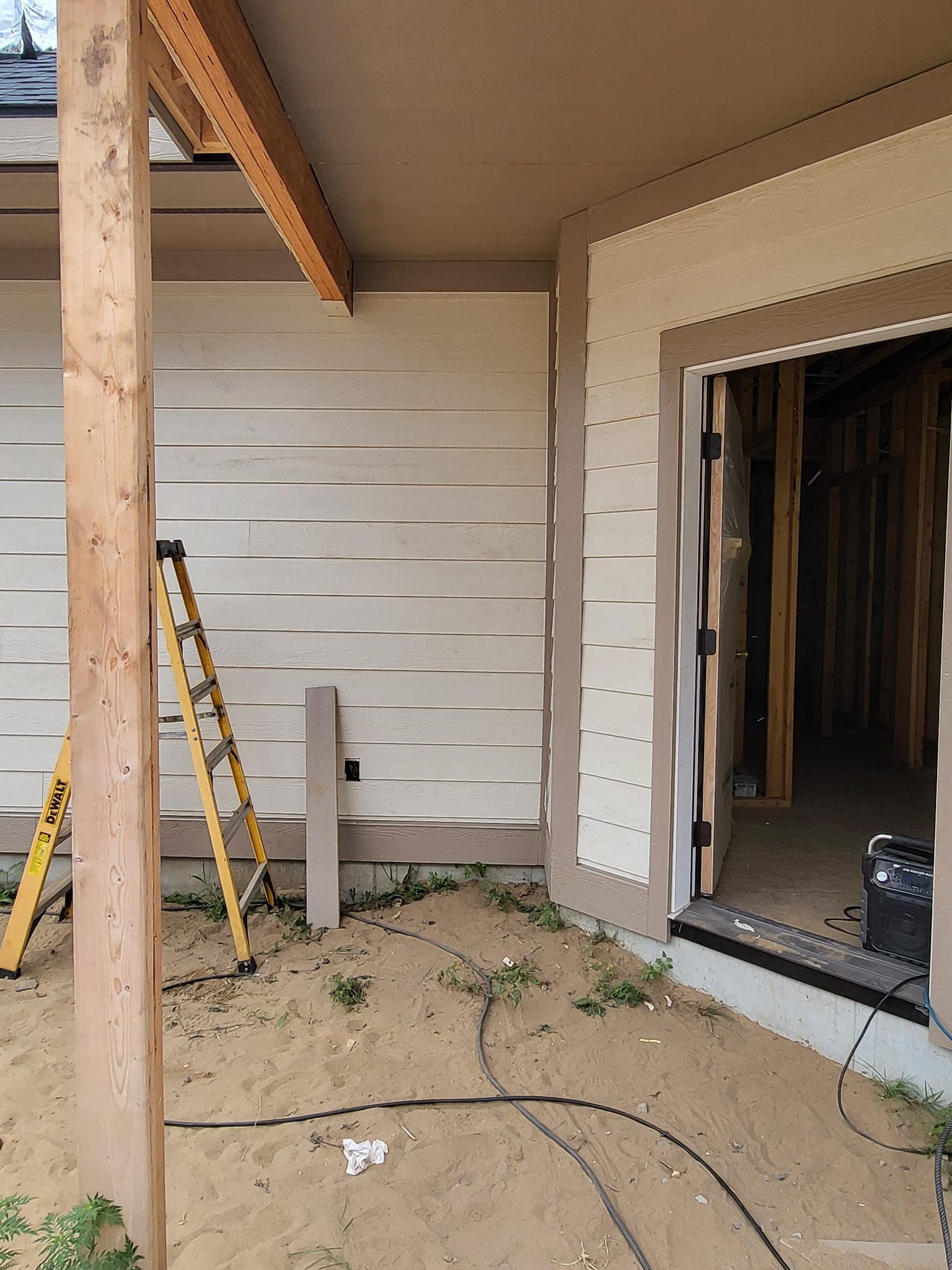 Partially finished patio with white siding, open doorway, and a ladder leaning against a post