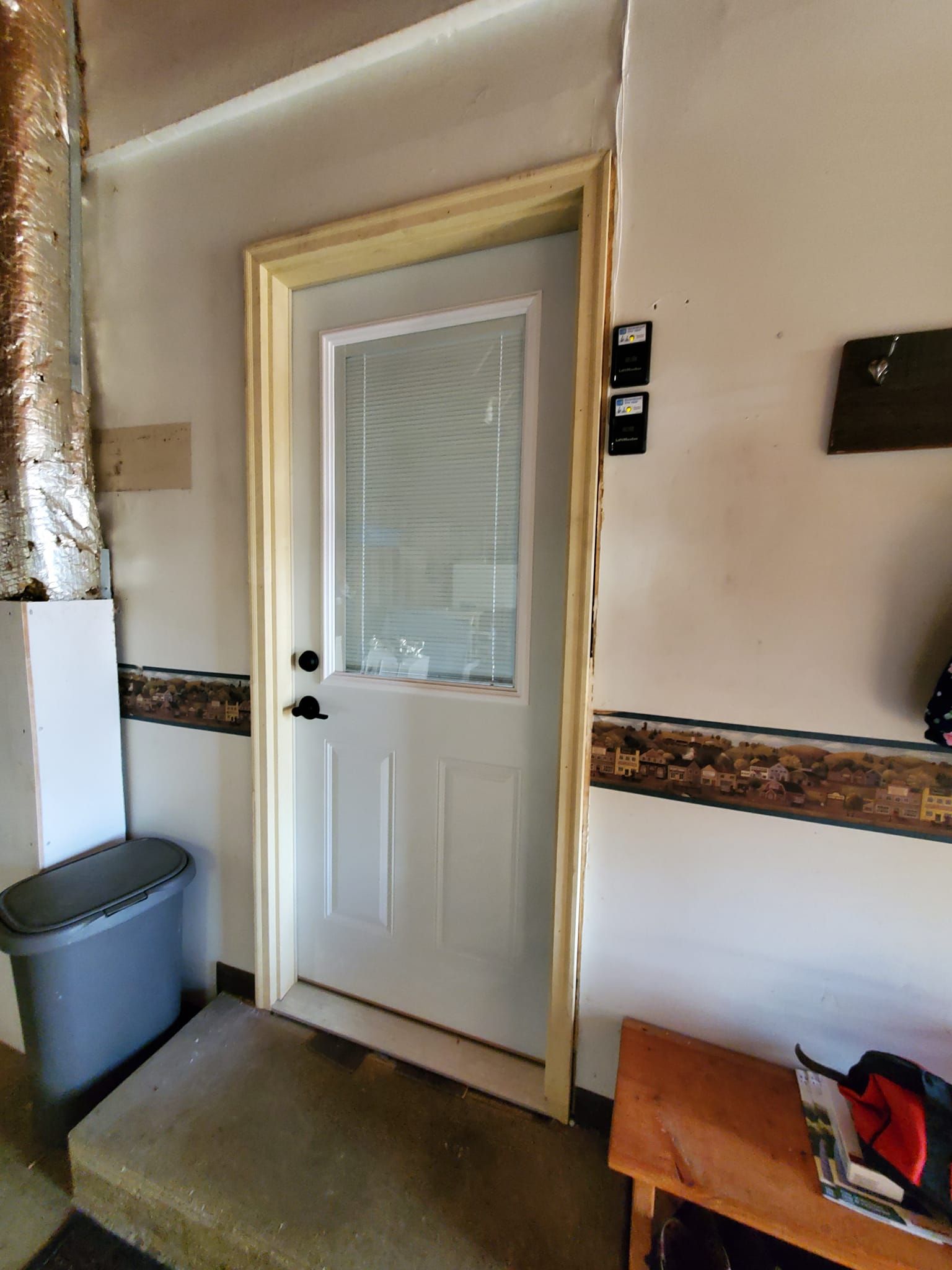 Interior doorway with a white door, small window, and hallway trim beside a trash bin and bench.