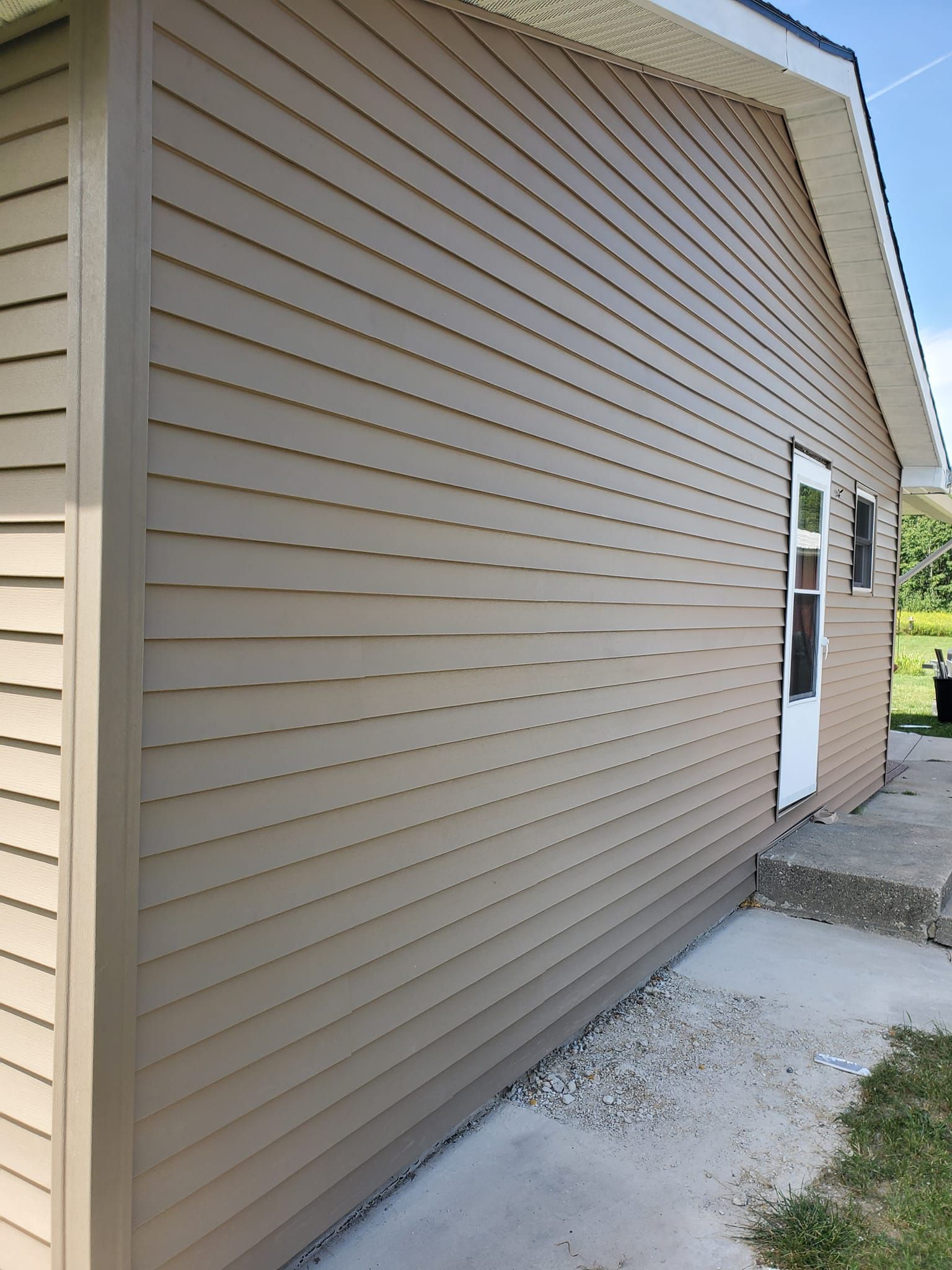 Tan vinyl-sided garage exterior with a side door, window, and concrete driveway.