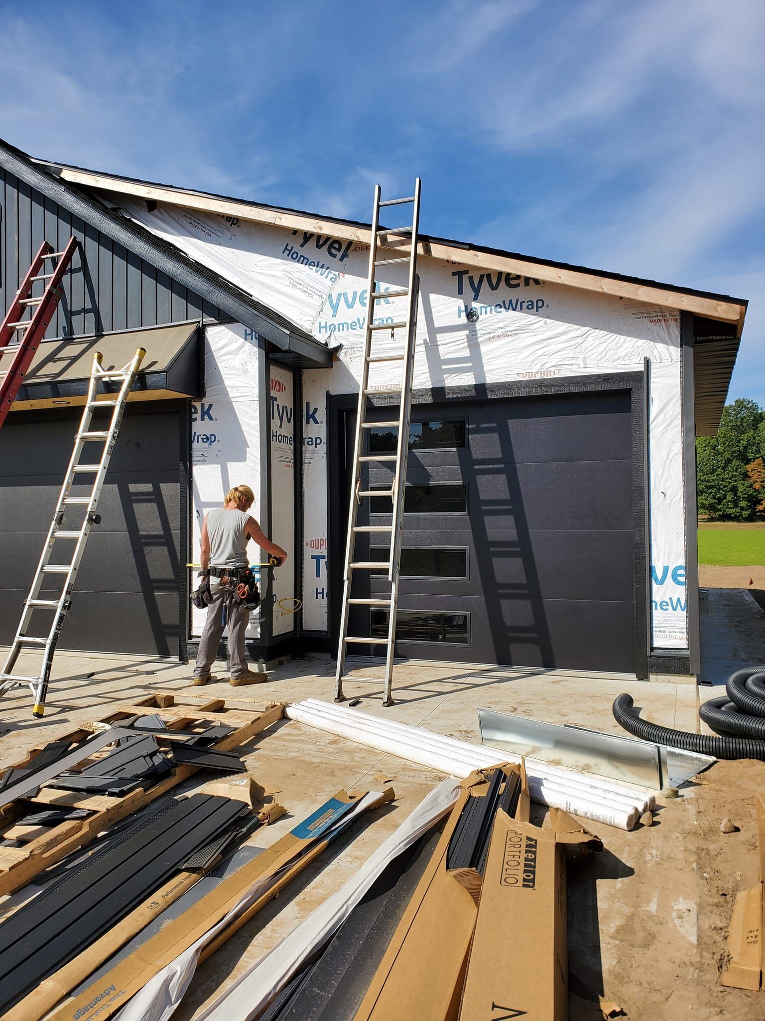 Two workers on ladders installing house siding and roofing on a partly finished building.