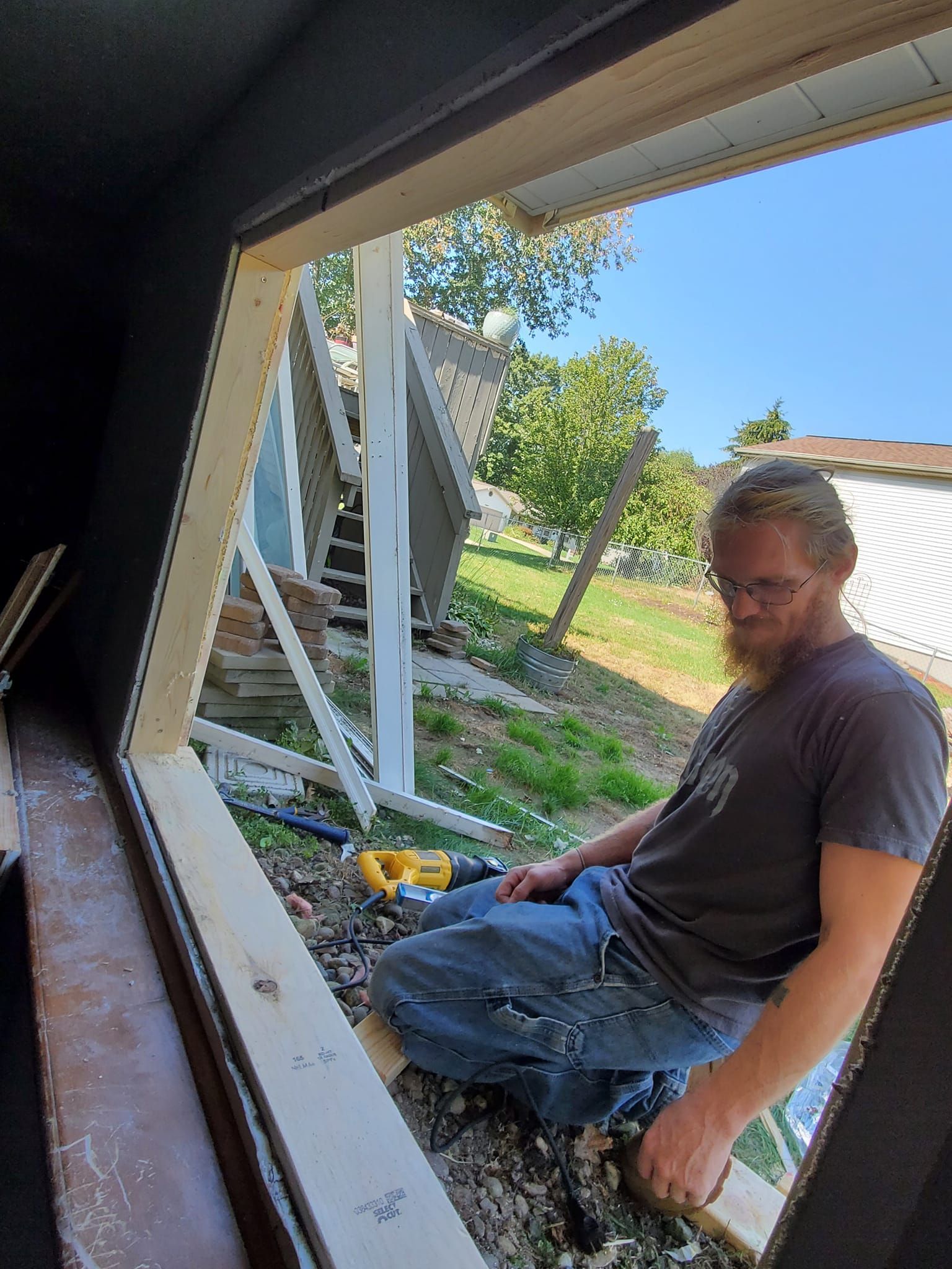 Man sitting on a window ledge beside a house opening, looking toward the camera.