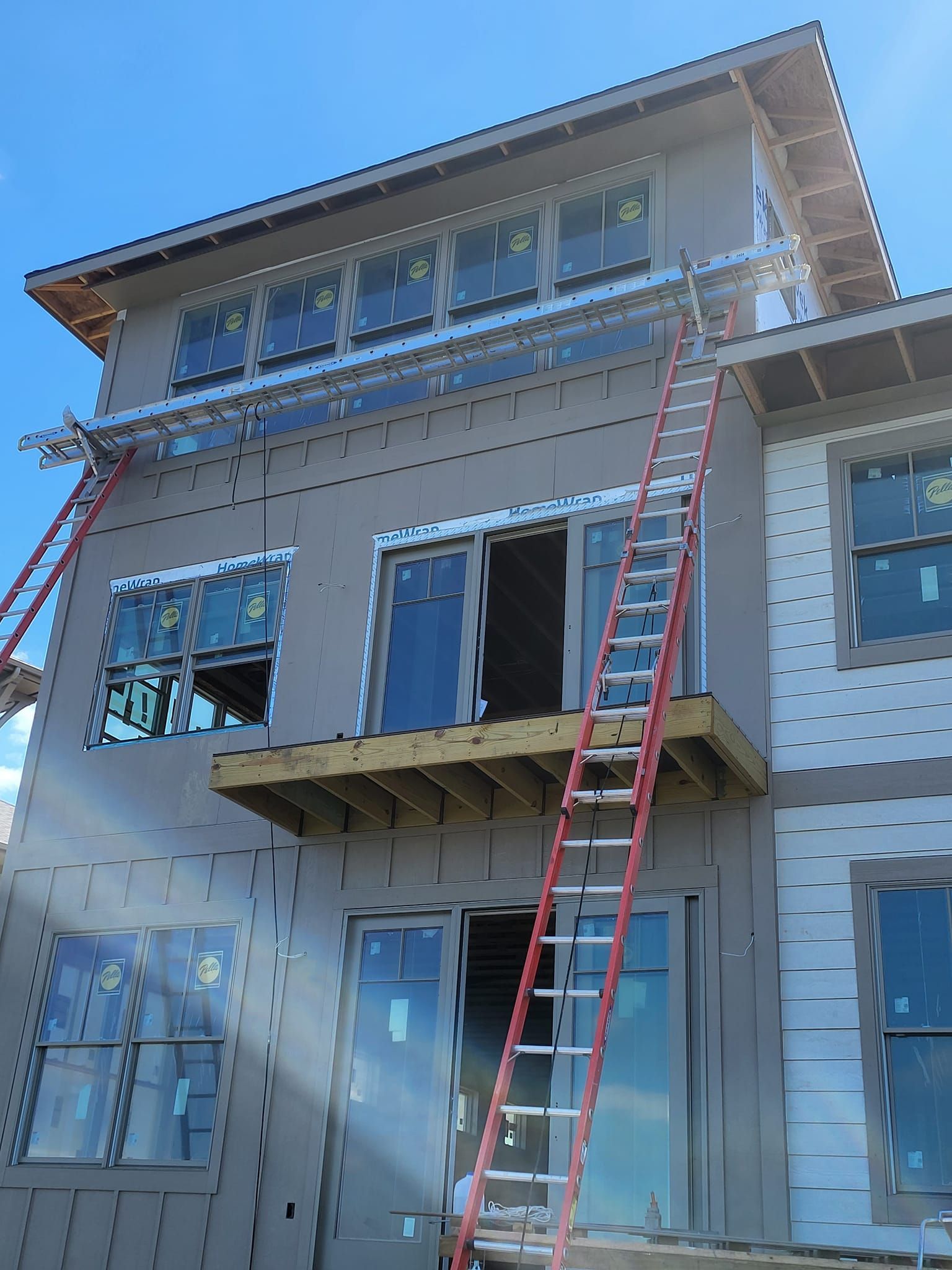 Three-story house under construction with ladders leaning against the exterior.
