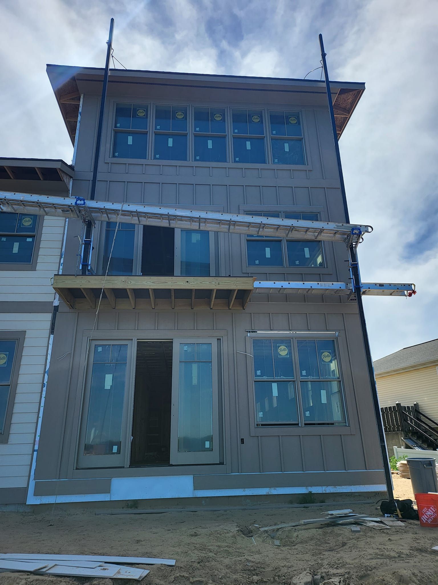 Three-story house under construction with gray siding and blue-tinted windows