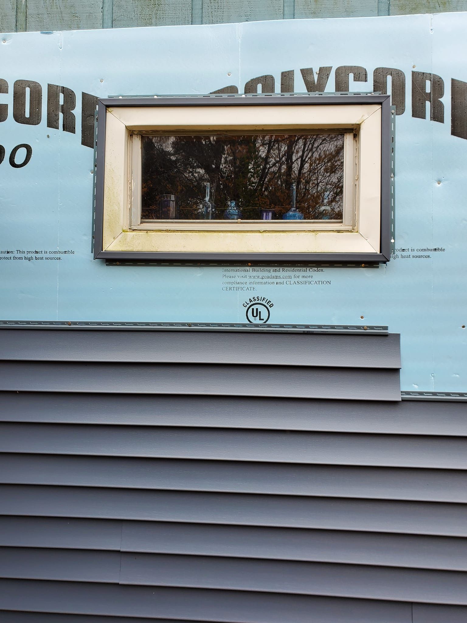 Small rectangular window on a blue-sided building with horizontal siding below it.