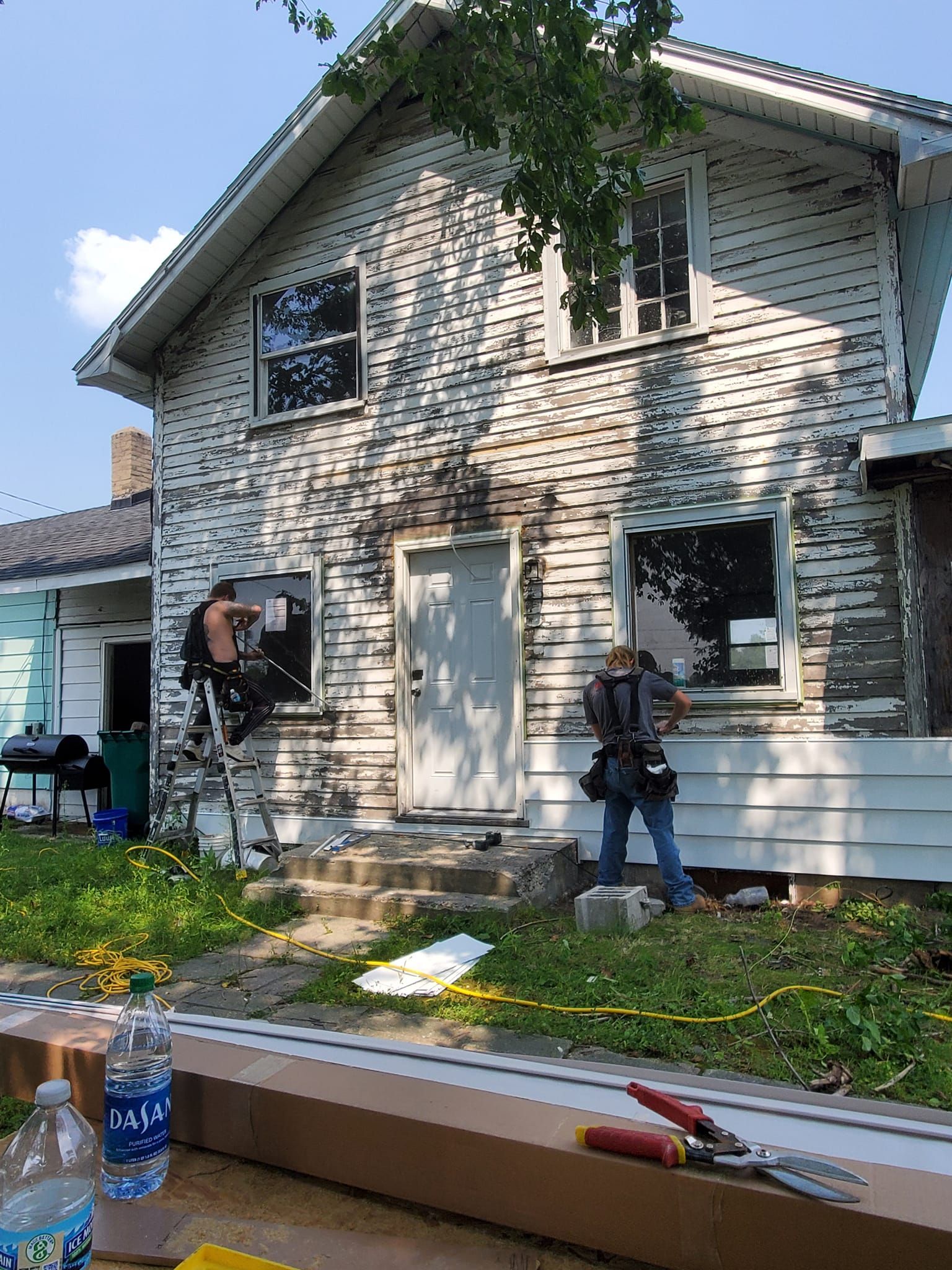 Workers painting the exterior of a white two-story house with ladders and paint supplies.