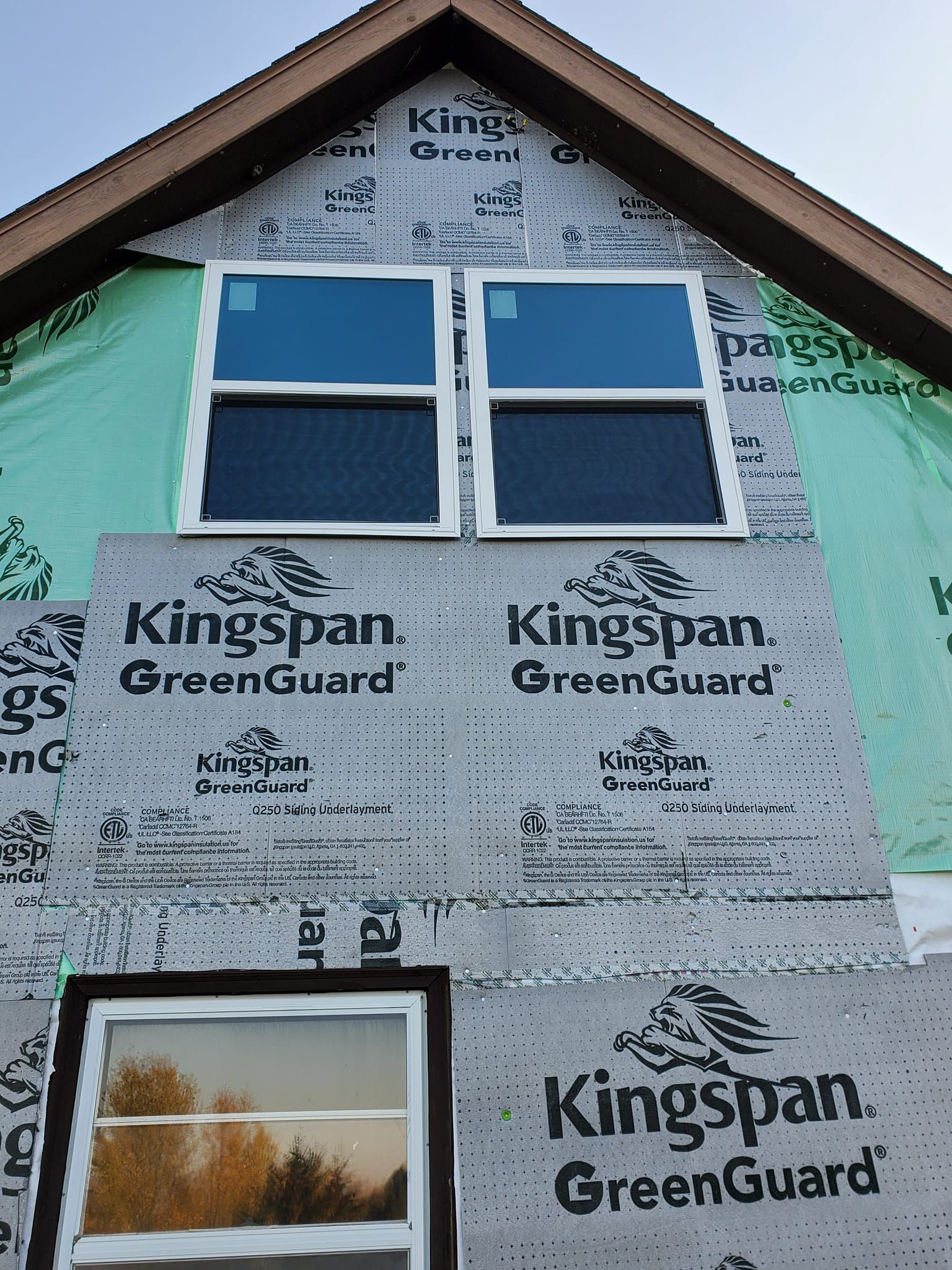 Partially finished house exterior with Kingspan GreenGuard insulation, blue-trimmed windows, and green wrap