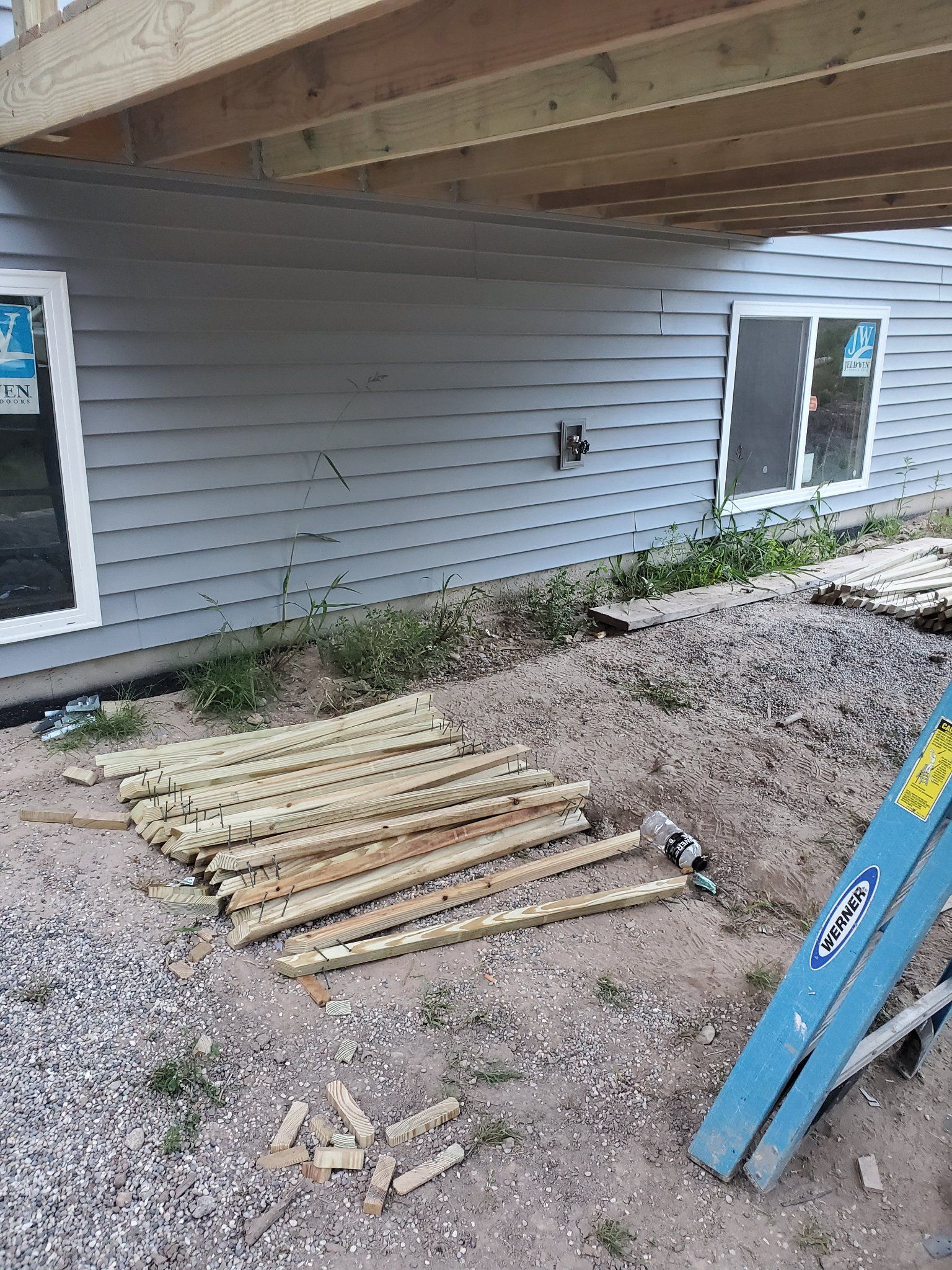 Damaged wooden ramp beside a house, with scattered debris and a blue ladder leaning nearby