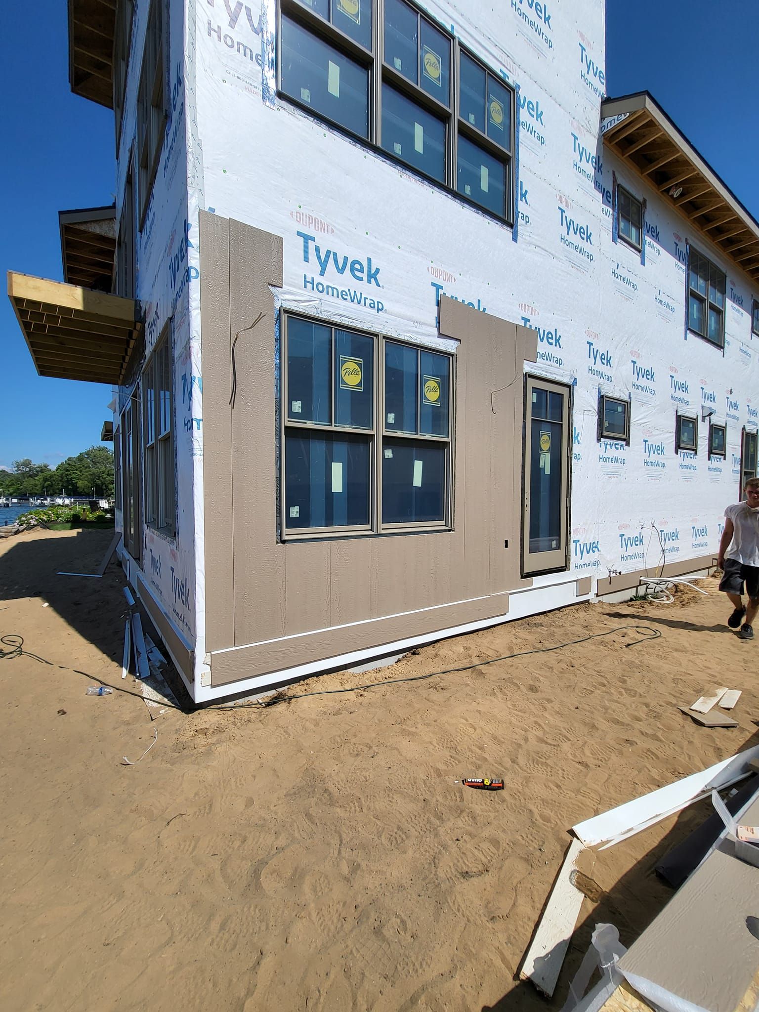 Partially built house exterior with blue siding, beige trim, and sandy ground under clear sky