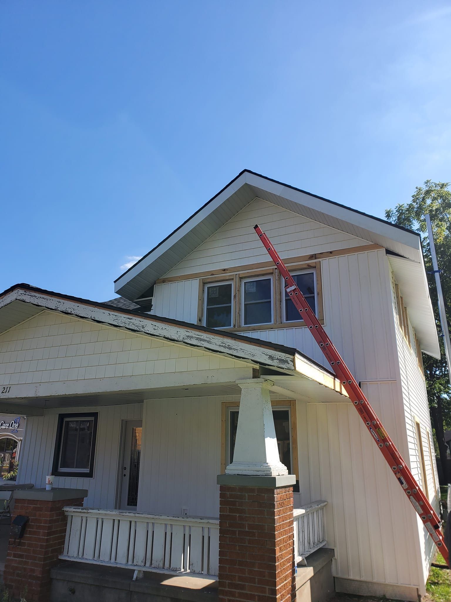 Two-story house with white siding, front porch, and red ladder leaning to the roof.