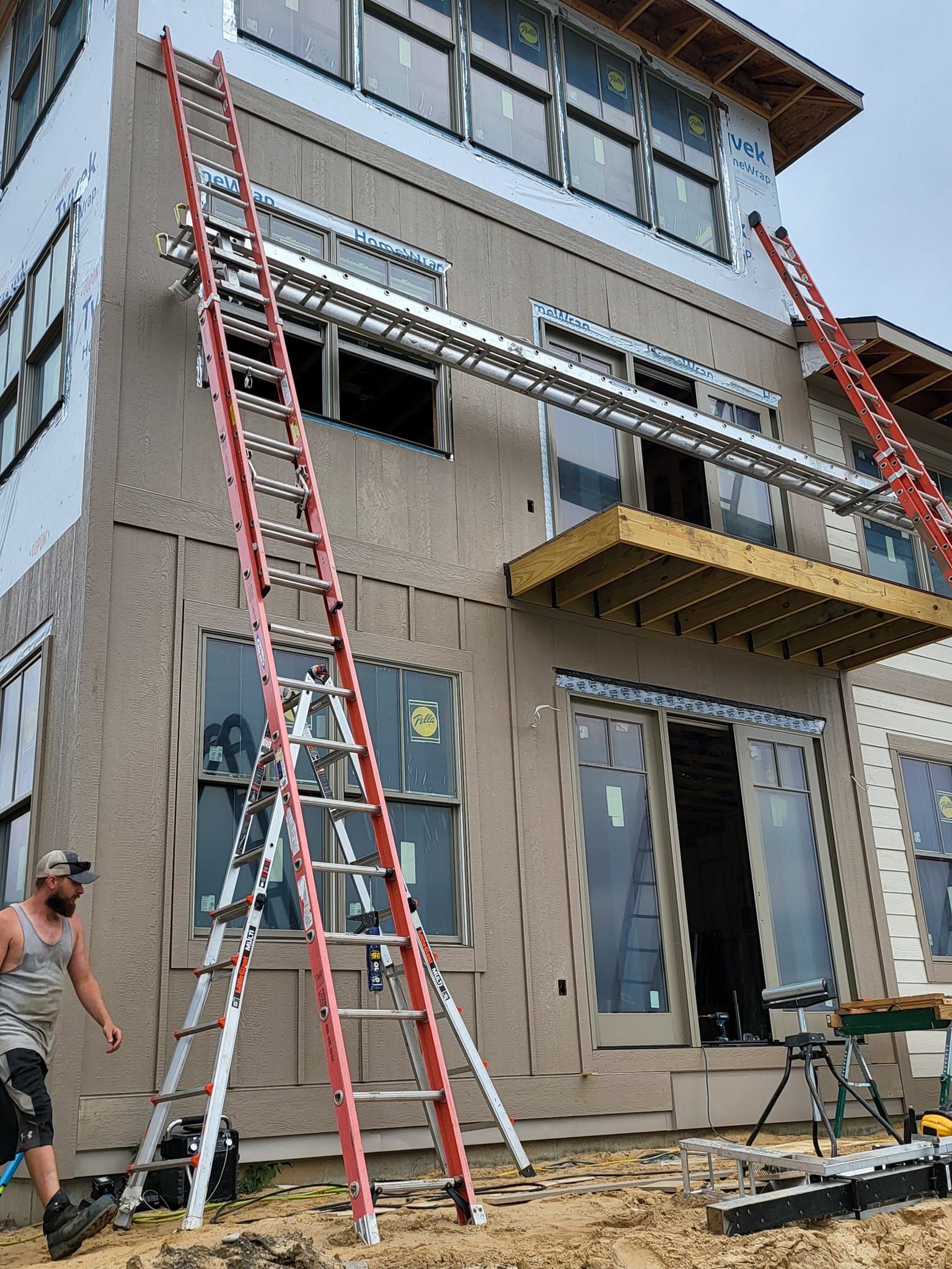 Workers on ladders painting a two-story house exterior with gray siding and unfinished front entrance.