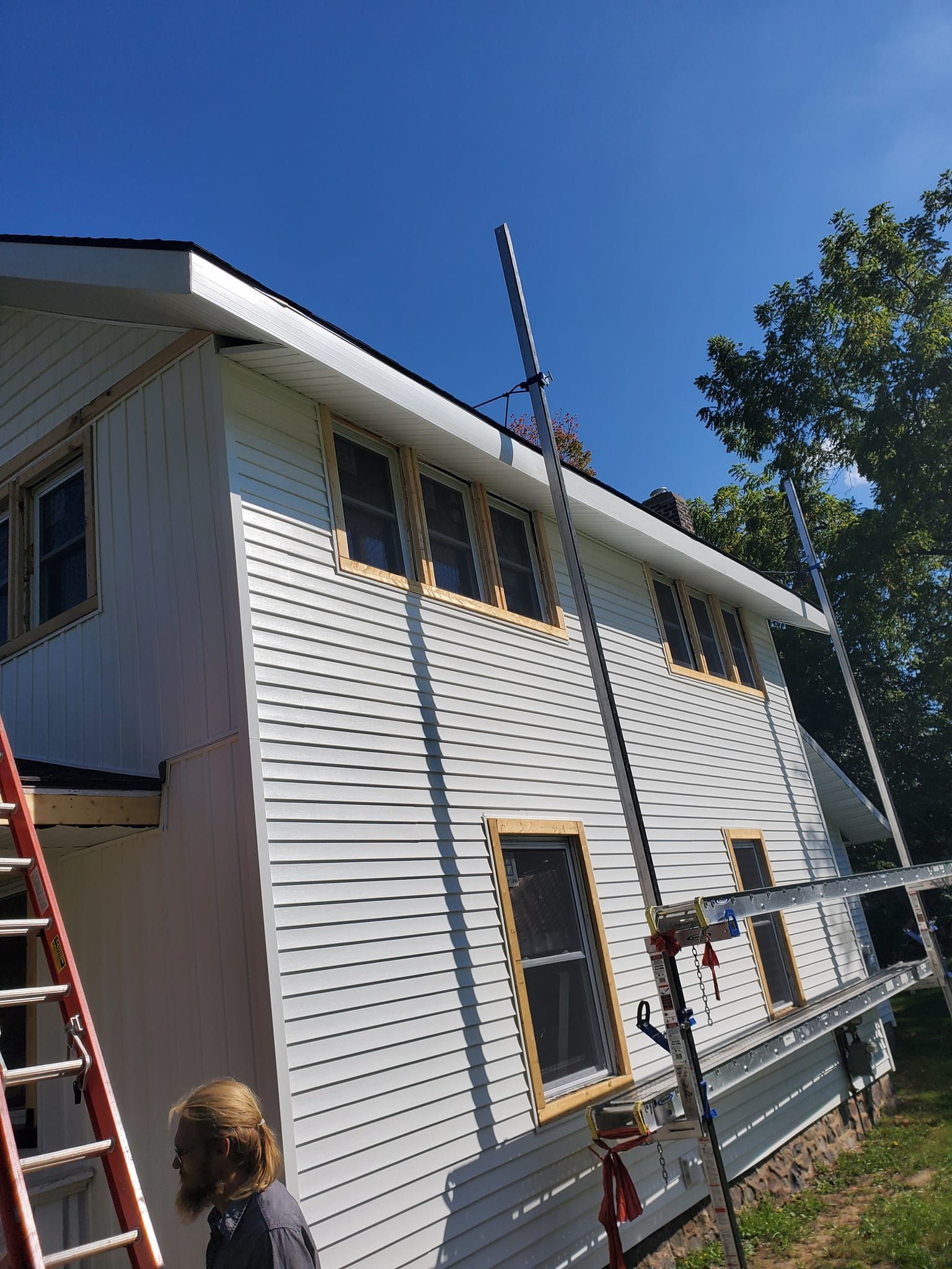Two-story white house under renovation, with ladders and scaffolding against the siding.