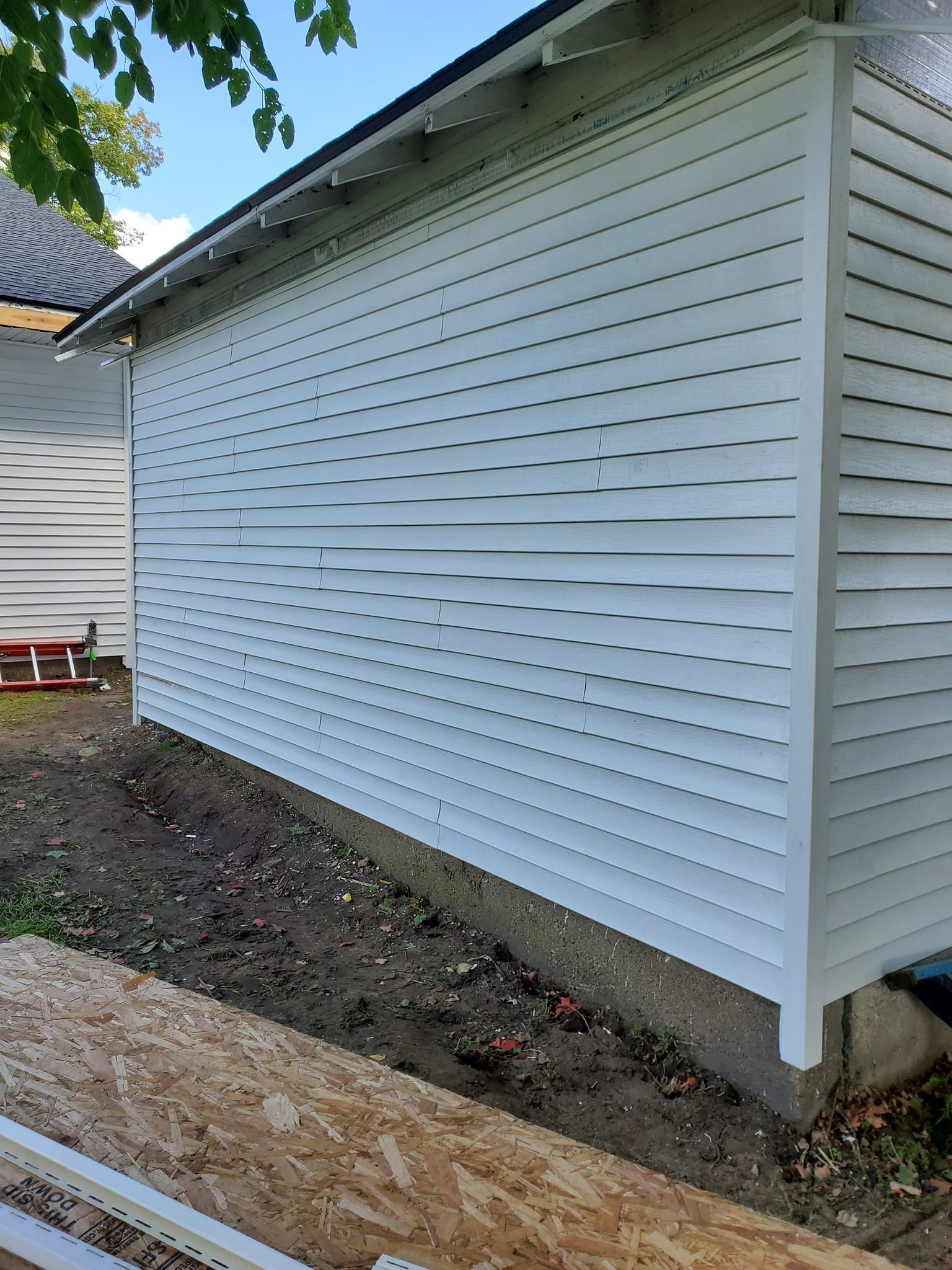 White house siding with visible horizontal dents above a dirt strip and concrete foundation edge