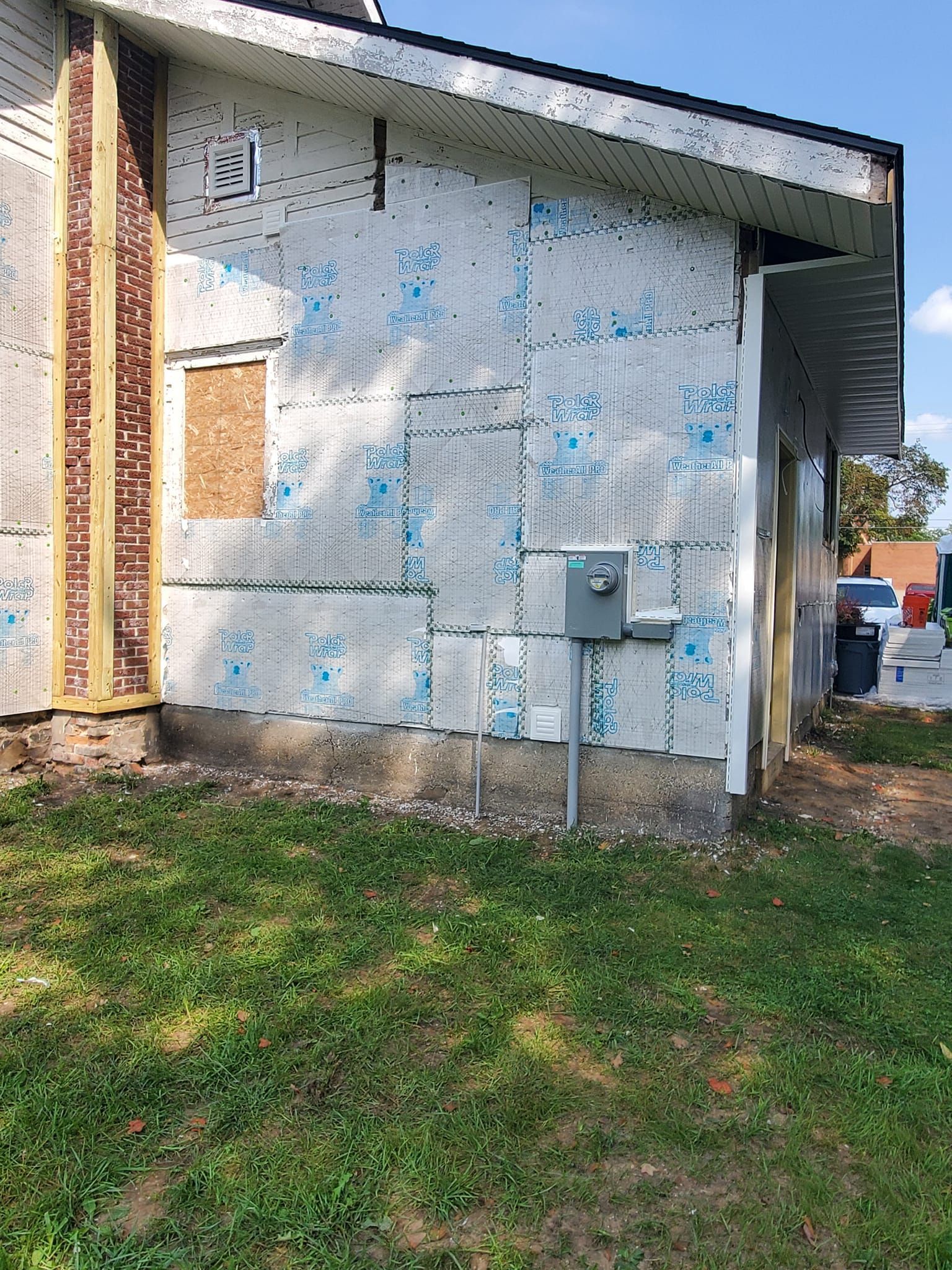 Exterior side of a small building with peeling white paint, utility boxes, and a grassy yard.