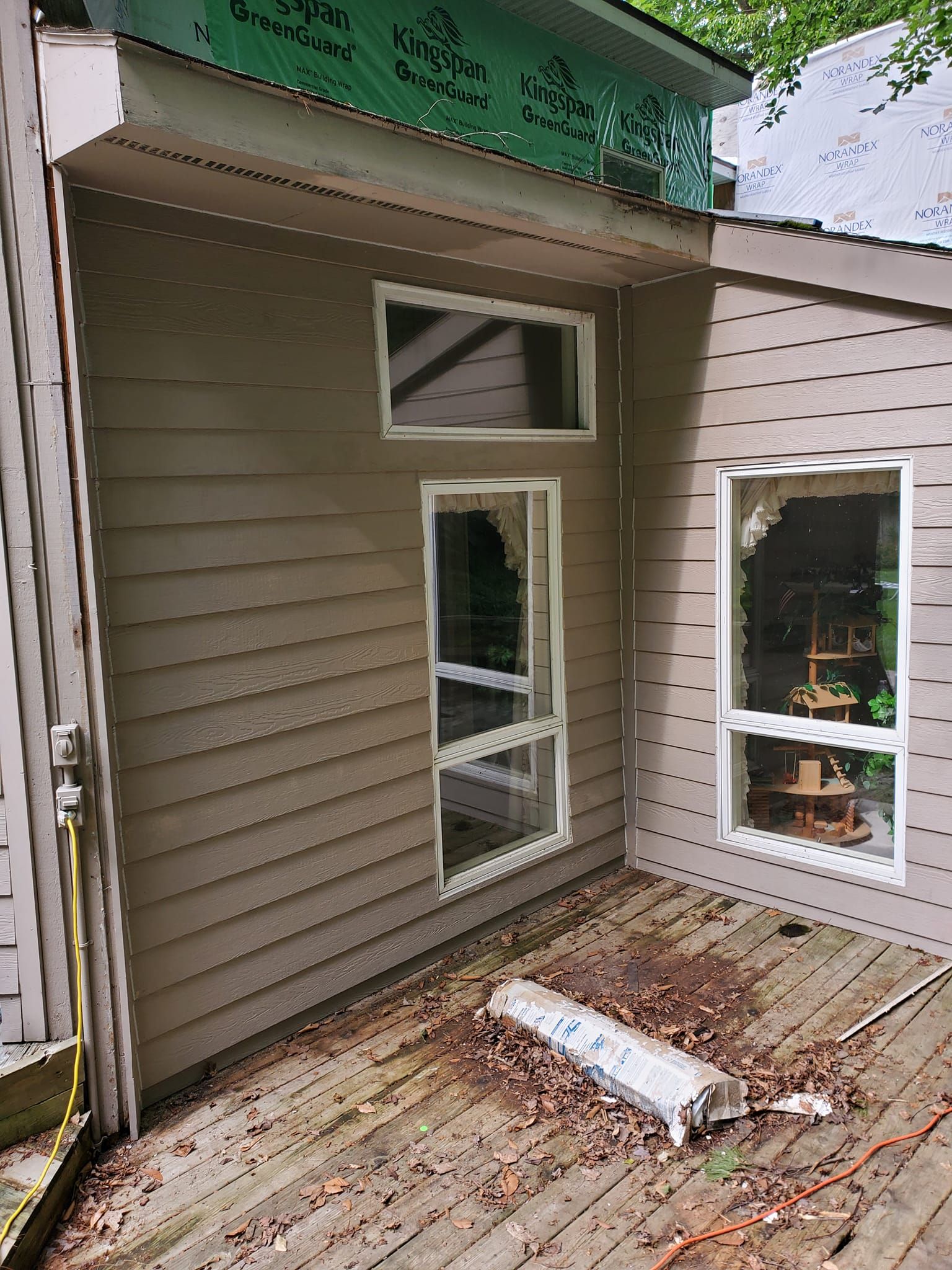 Exterior wall with two windows and a small weathered wooden deck with scattered debris.