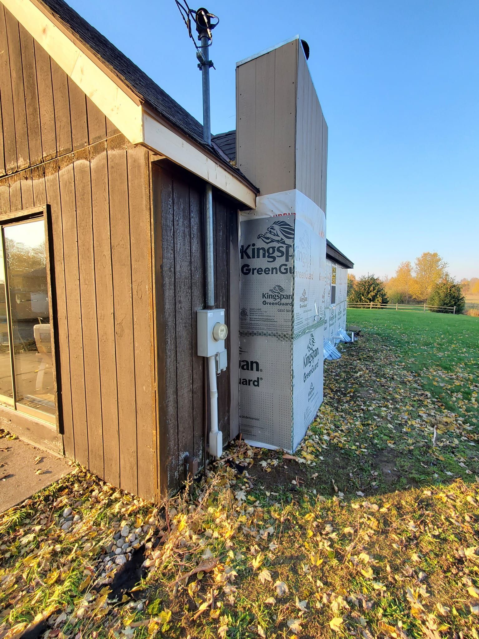Partially built wooden house with foam insulation panels beside a grassy field in autumn