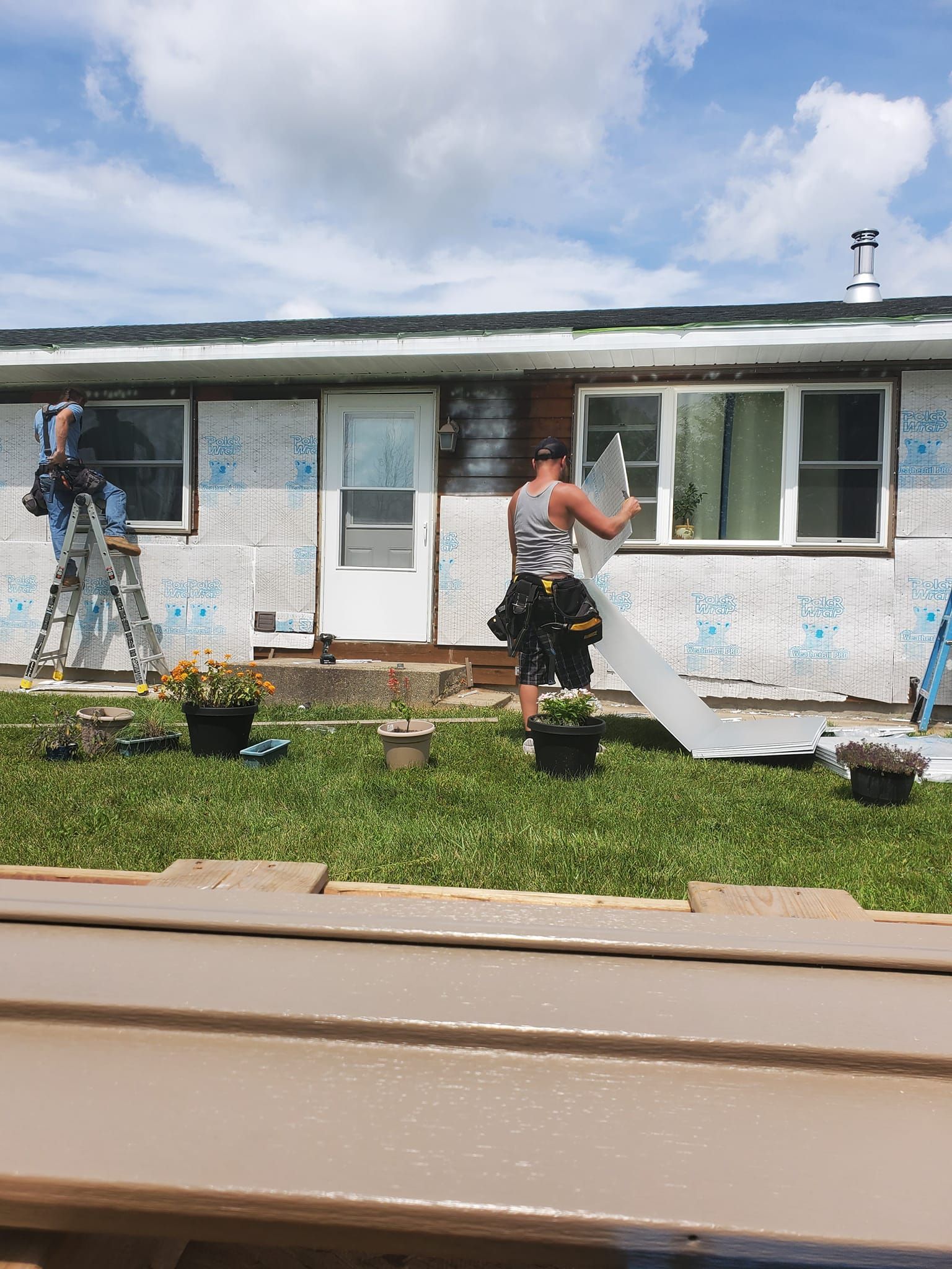 Workers painting the exterior of a white house with ladders and buckets in the front yard