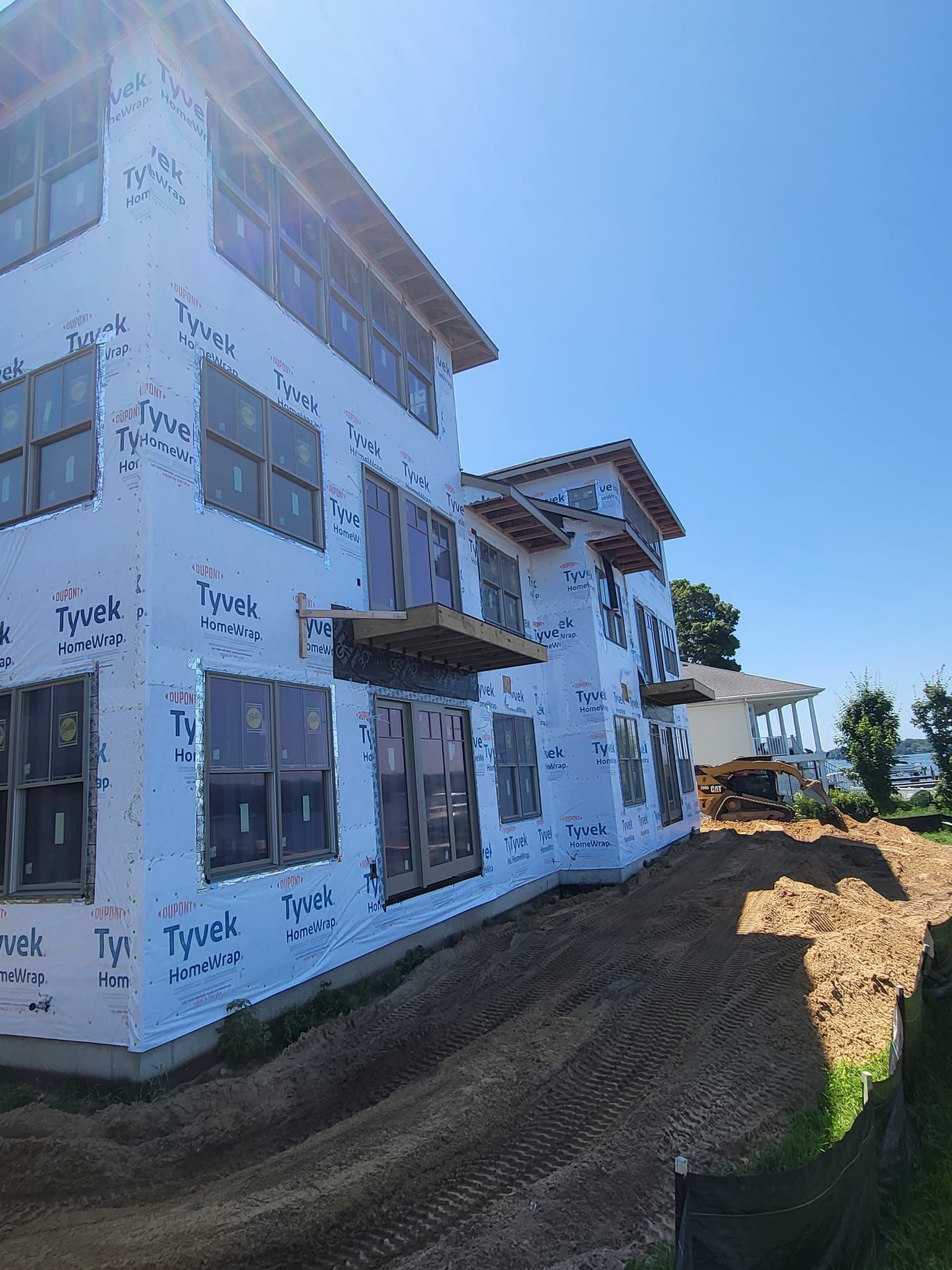Partially finished white house with exposed wrap and a muddy dirt driveway under construction