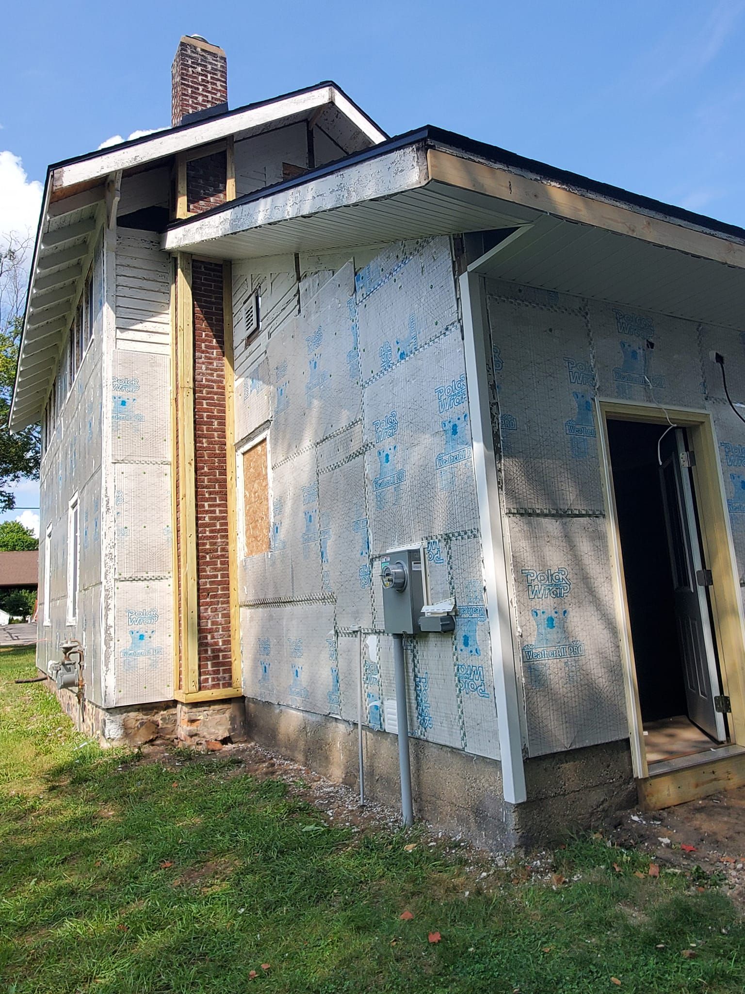 Dilapidated white house with peeling paint, boarded doorway, and overgrown grass outside.