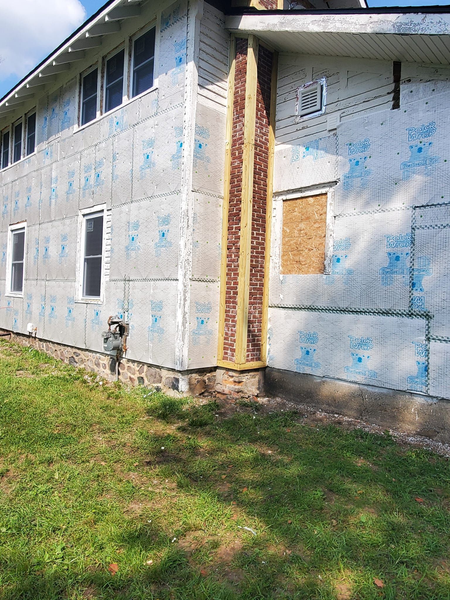 Weathered white building with blue markings, boarded window, and grassy foreground