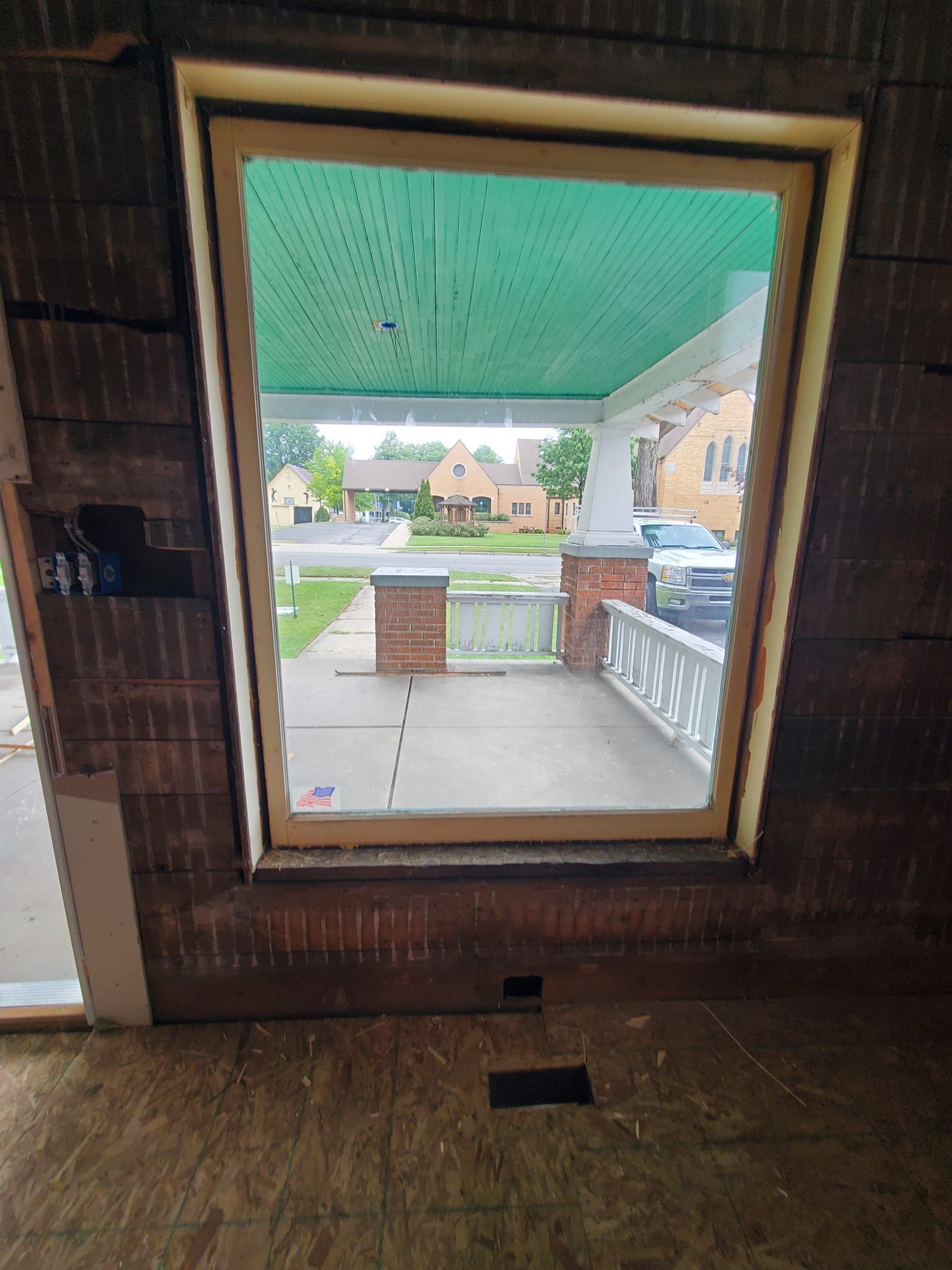 View through a large window to a covered porch with green ceiling and street beyond