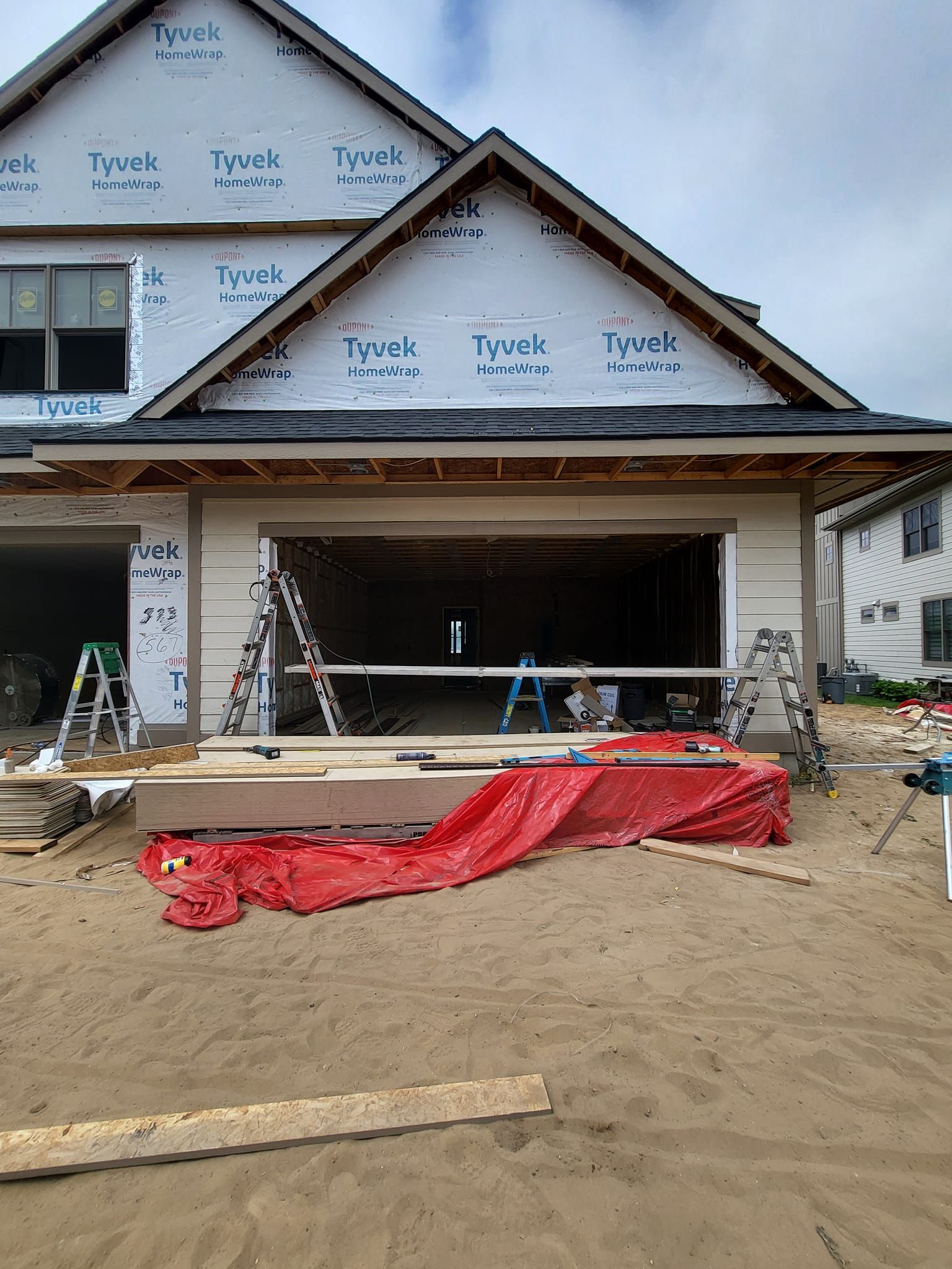 New house under construction with open garage, ladders, and red tarp on the ground