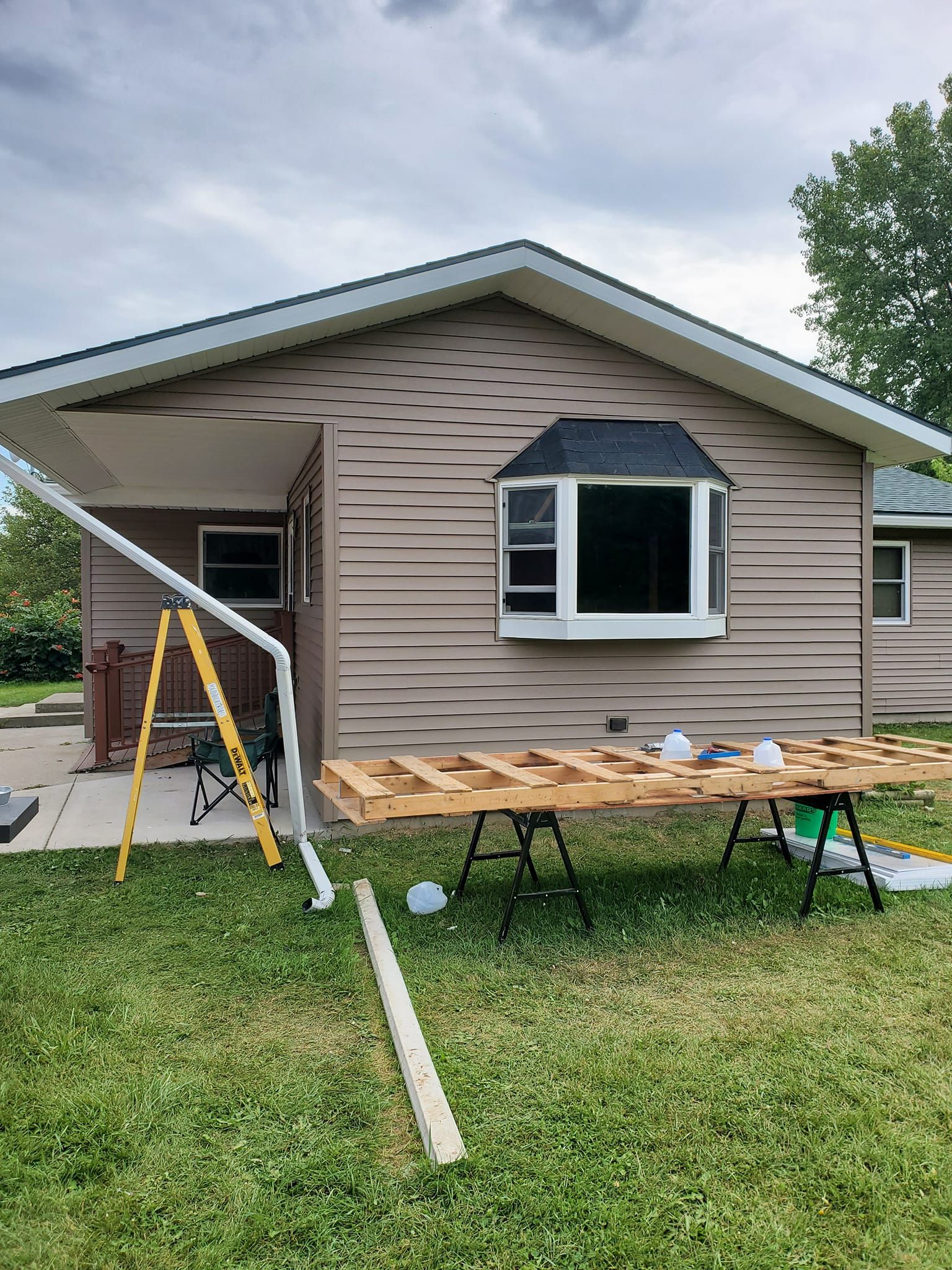 Single-story house with new siding; ladder and sawhorses in the front yard.