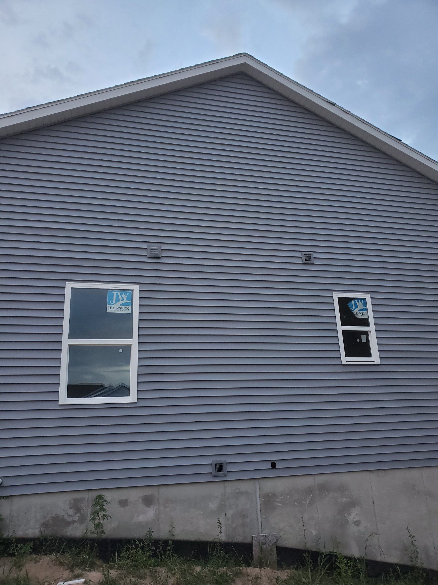 Side of a gray house with two windows and vinyl siding under a cloudy sky