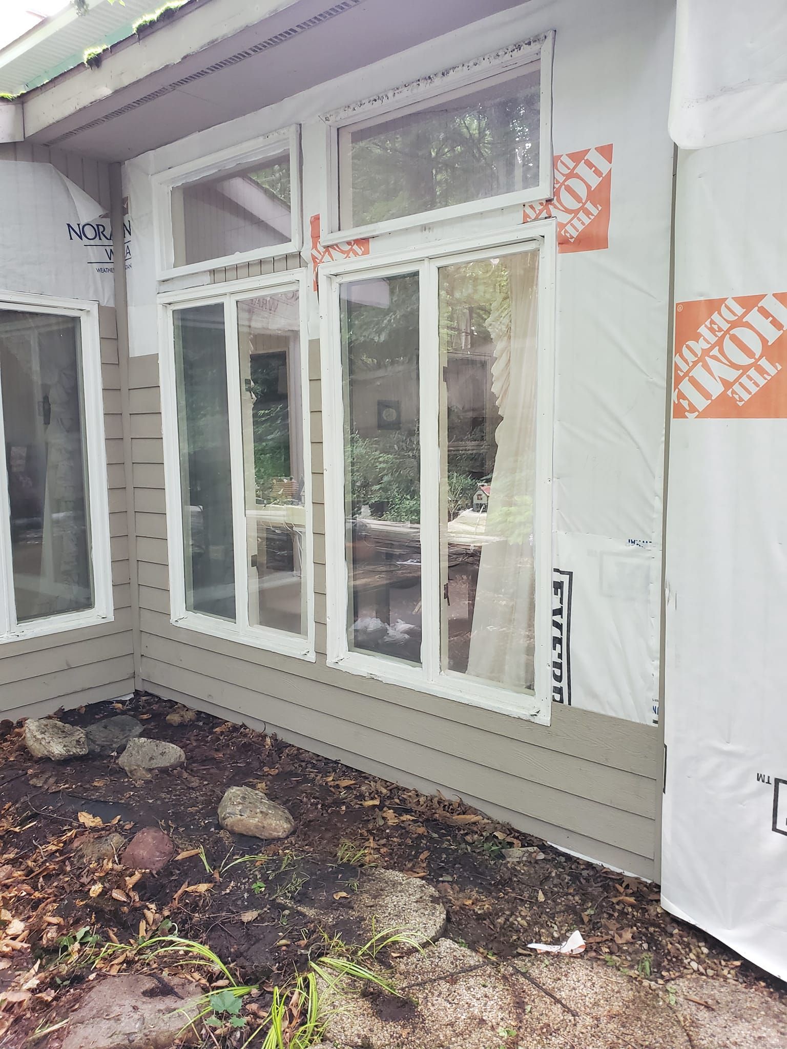 Covered porch with white French doors and windows under construction, wrapped in house sheathing.