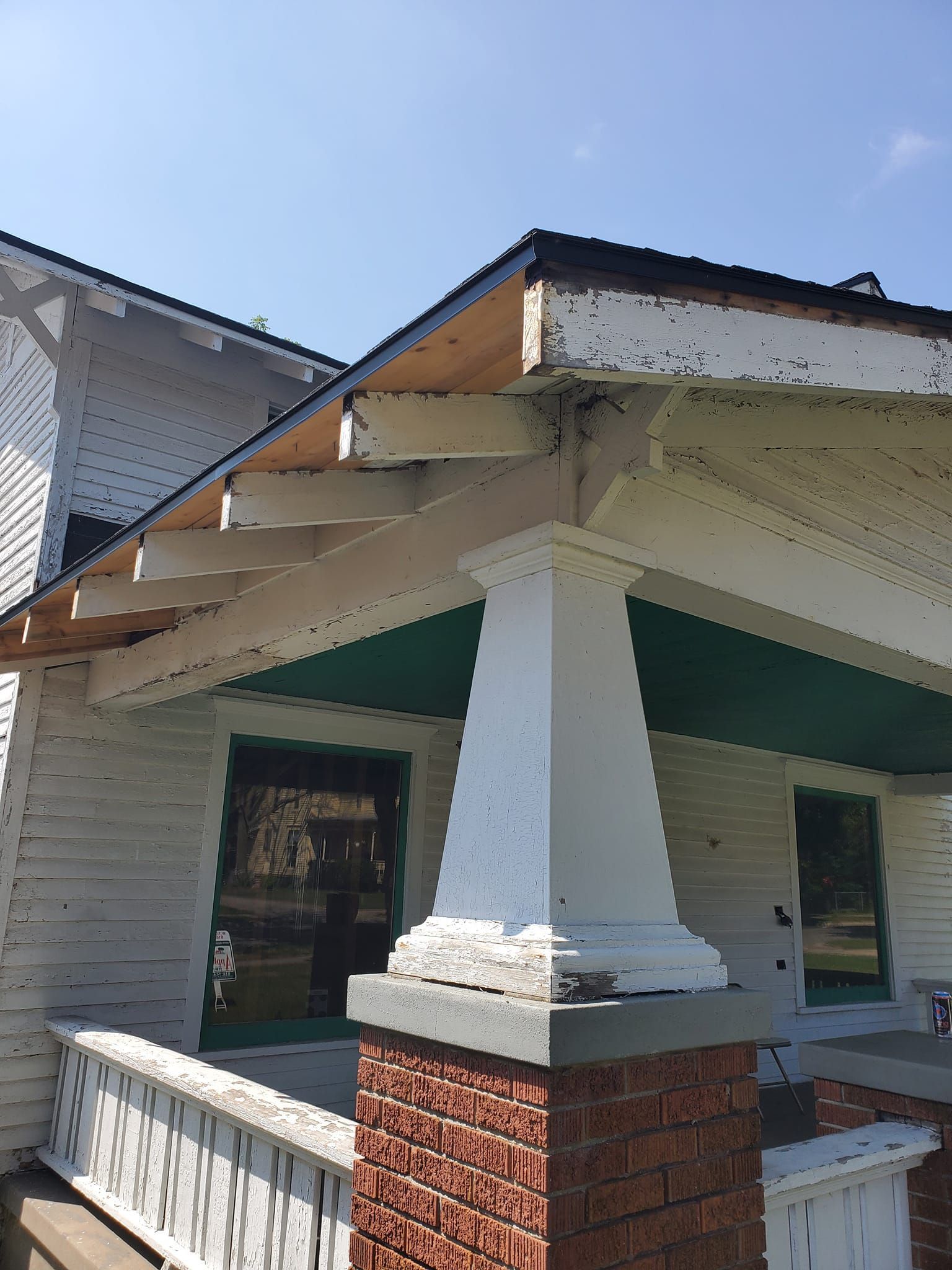 Front porch of a house with white columns, brick trim, and a sloped roof under a blue sky