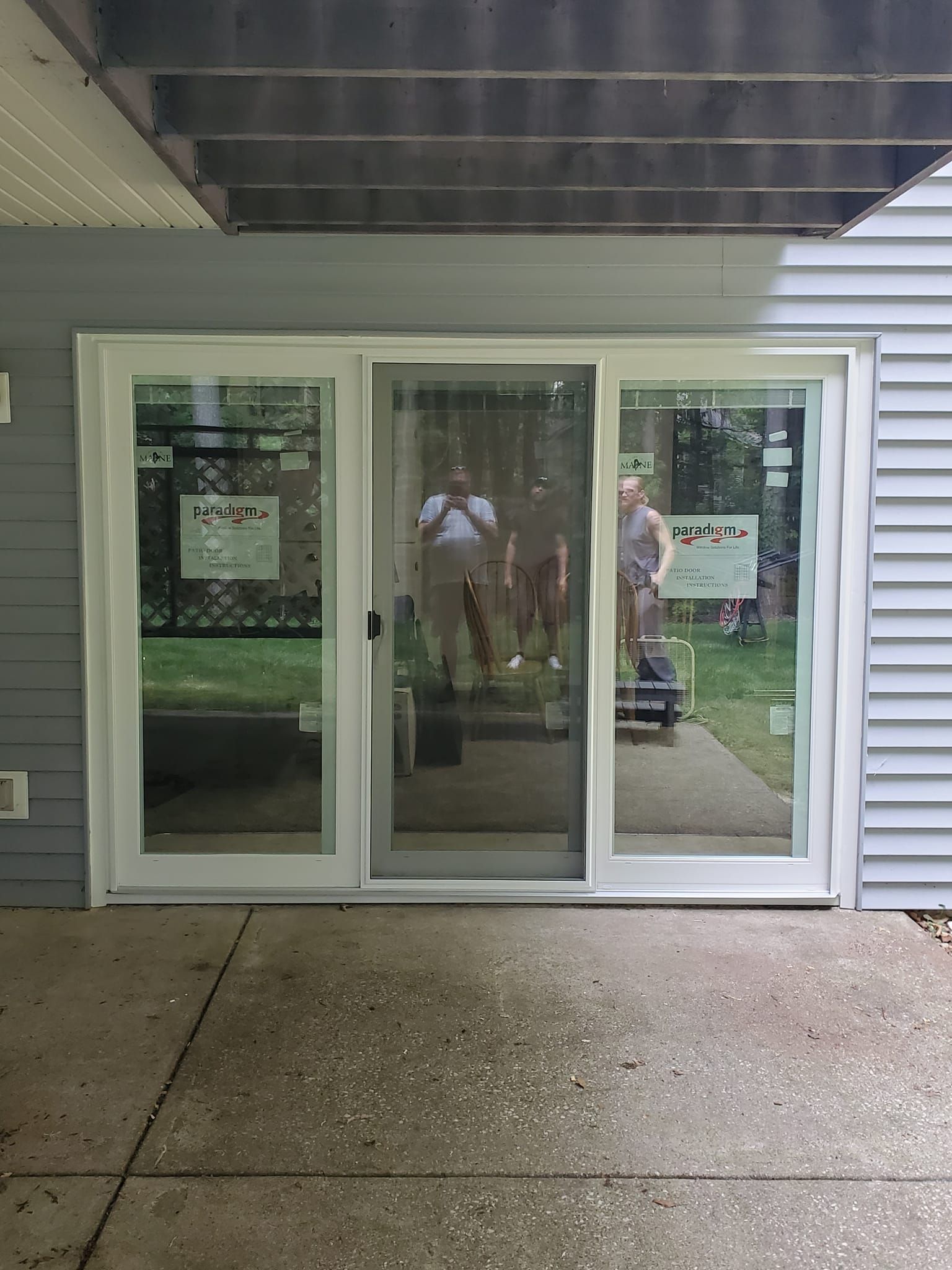 Sliding glass patio doors under a covered porch, with gray siding and wet concrete outside.