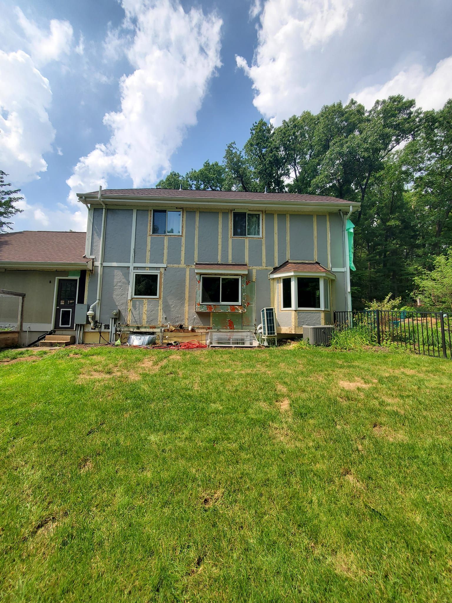 Two-story house with weathered siding and a small porch, viewed from a grassy yard under a blue sky.