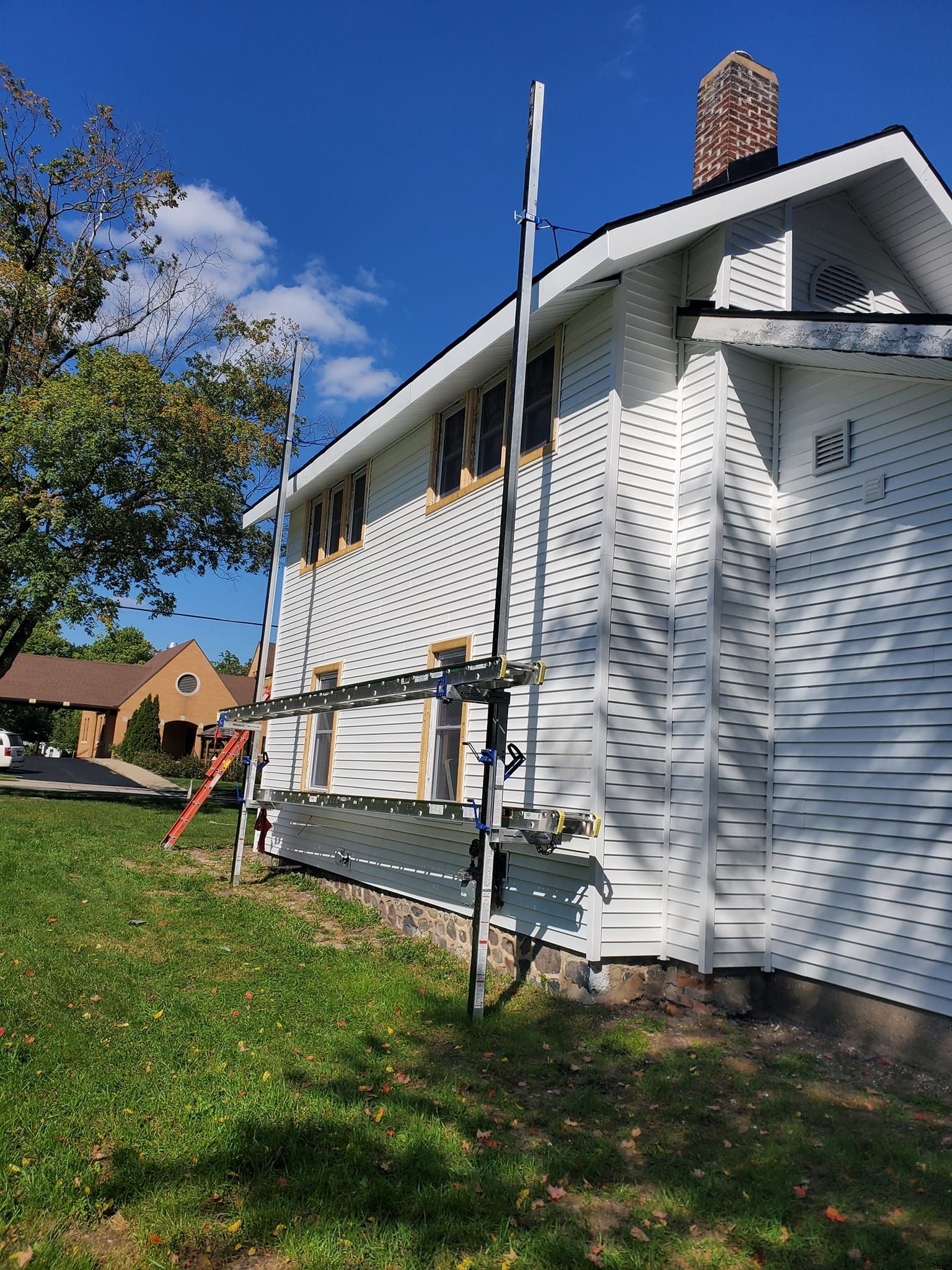 House exterior with white siding and scaffolding beside a green lawn under a blue sky