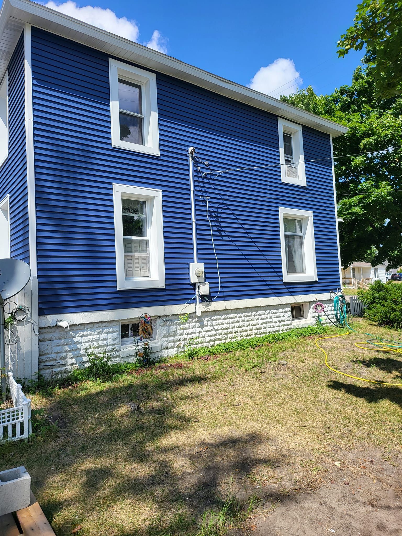 Blue two-story house with white trim and a small yard in bright sunlight