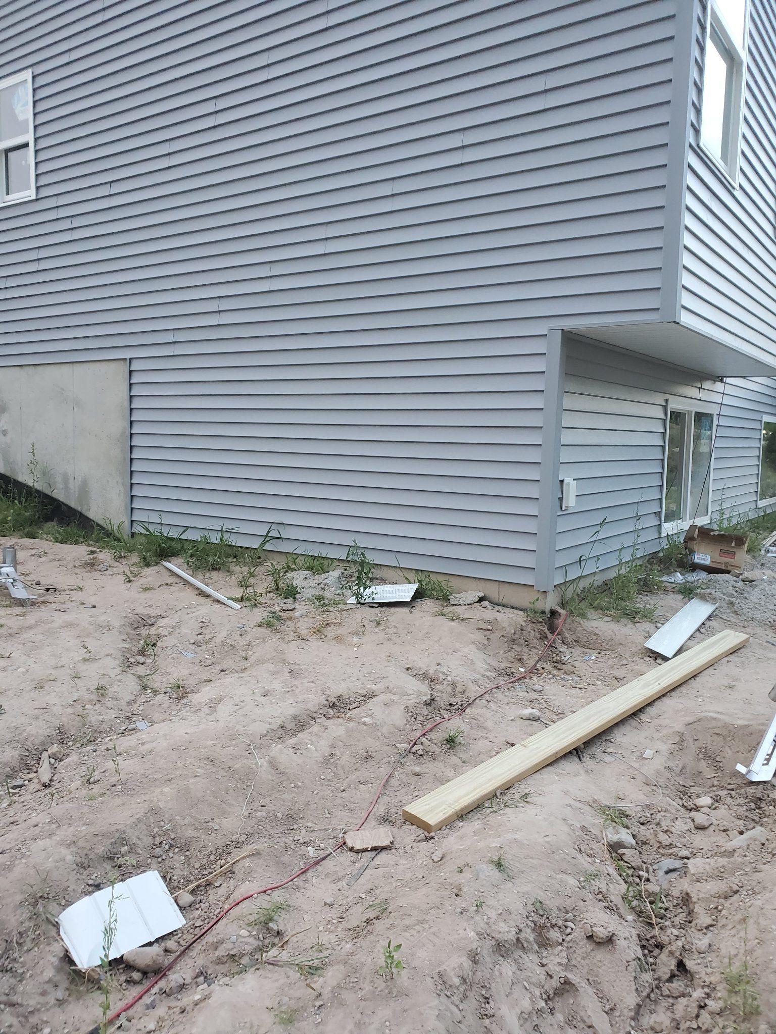 Side of gray house with dirt lot, scattered construction debris, and a small covered entryway