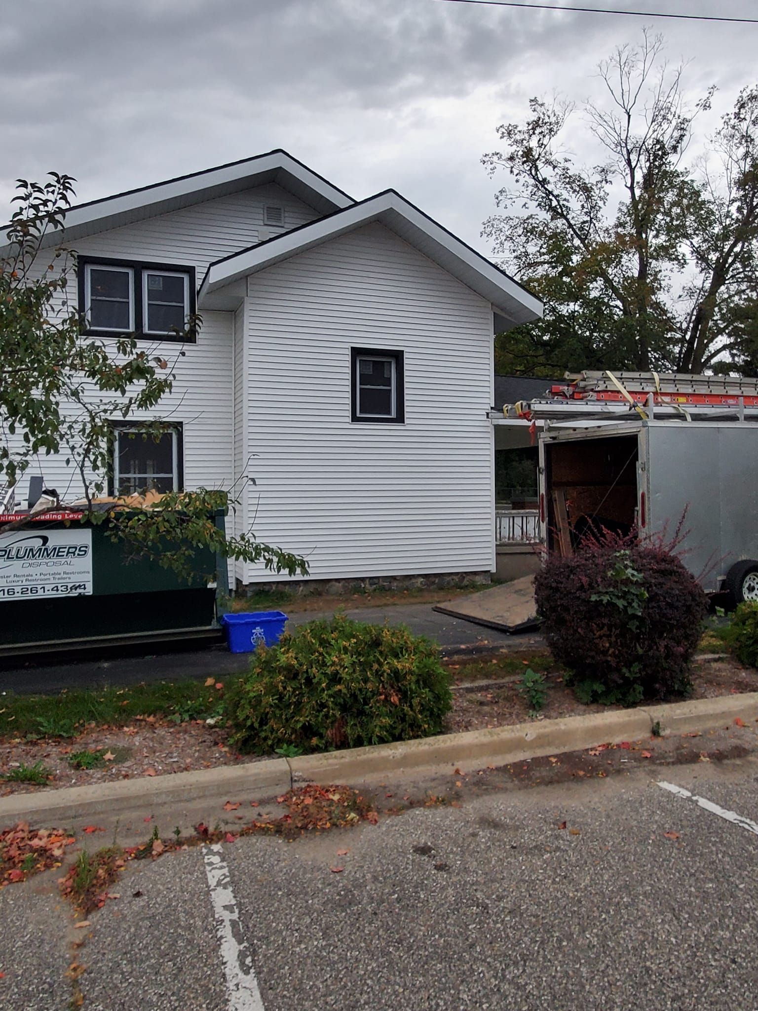 Small white house with gray roof, a window box, and a detached garage in an overcast neighborhood.