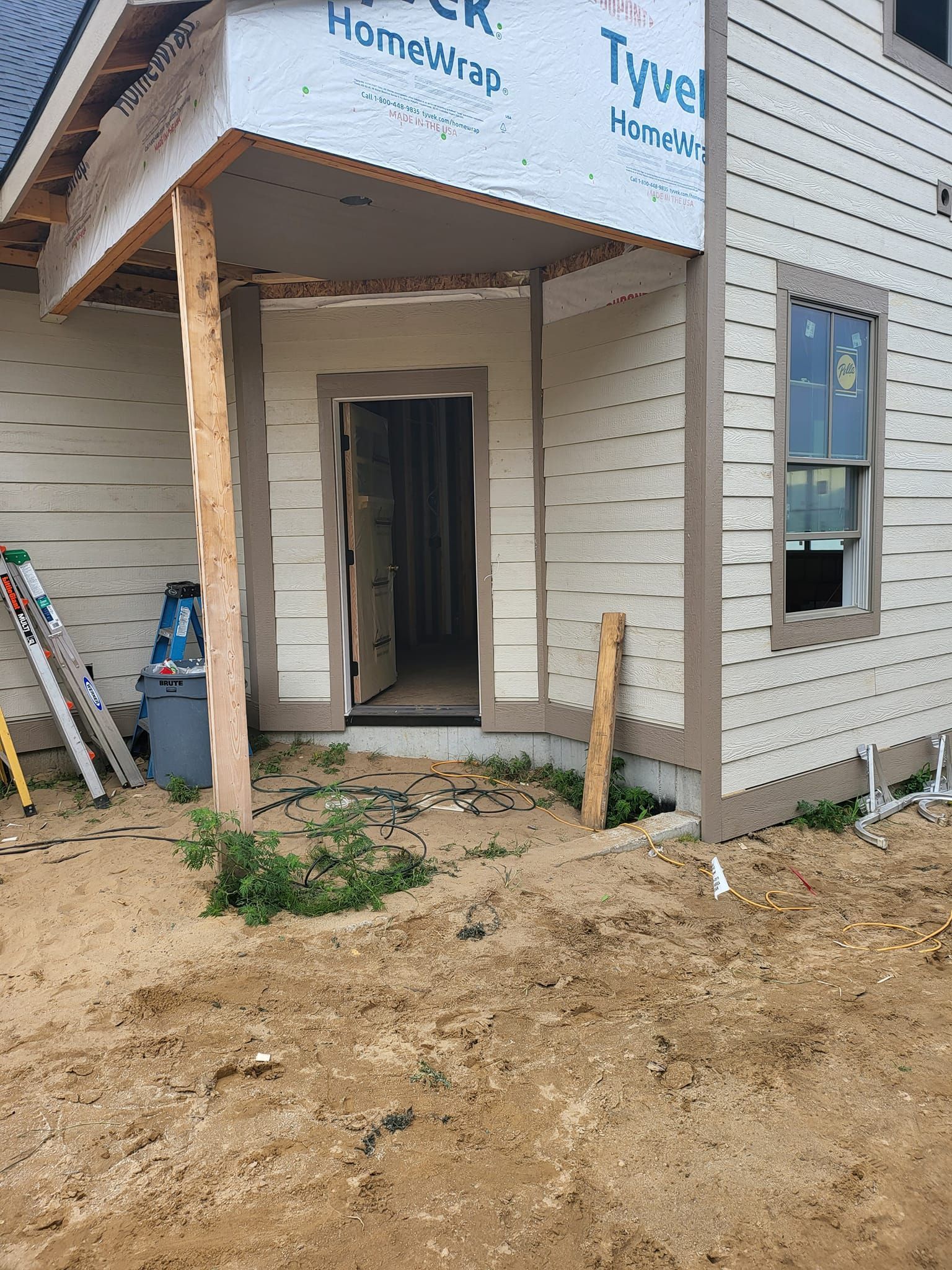 House entrance under construction with temporary wood support, open doorway, and siding partially installed.