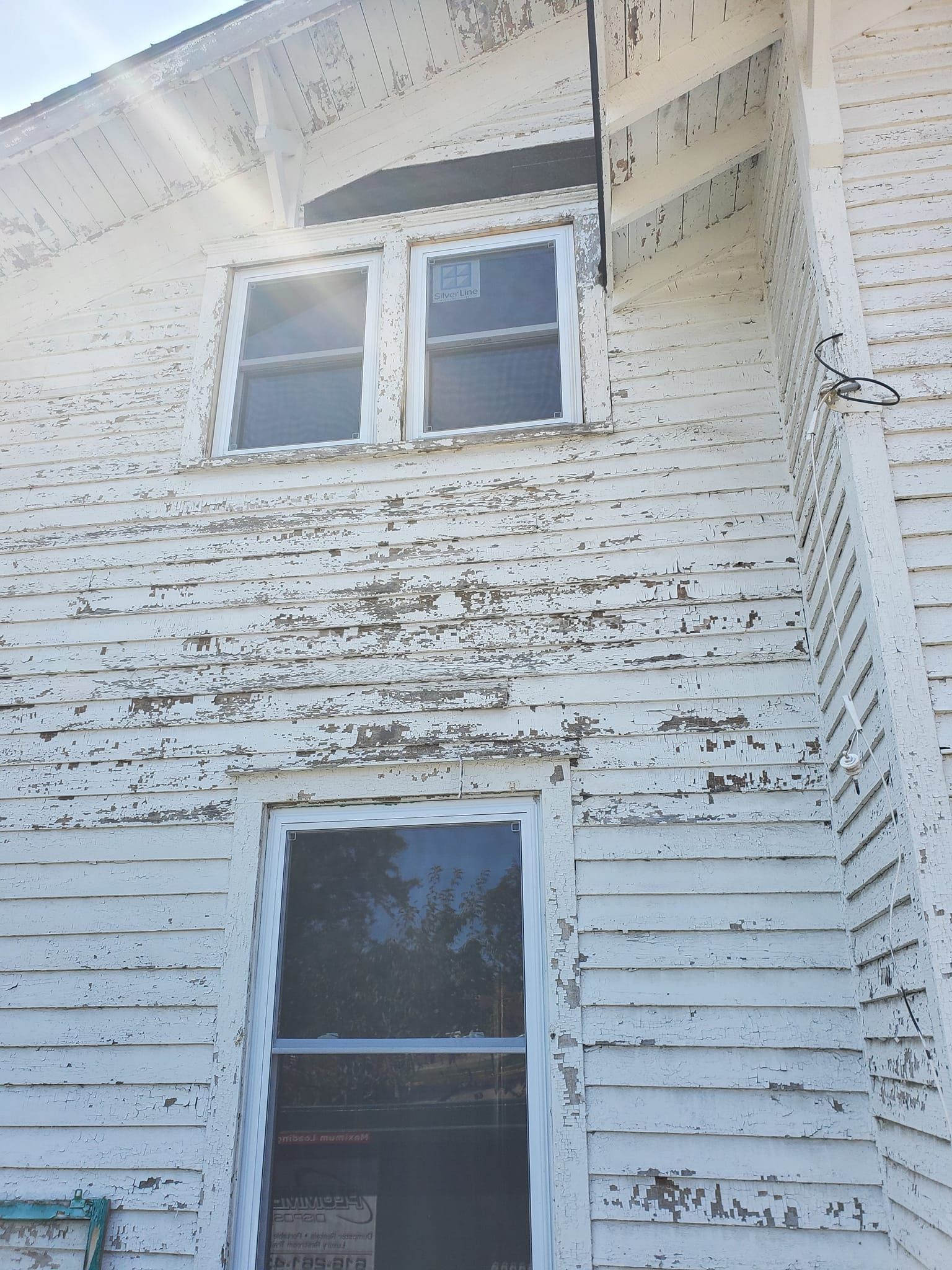 Weathered white house exterior with two windows and peeling paint beneath the eaves