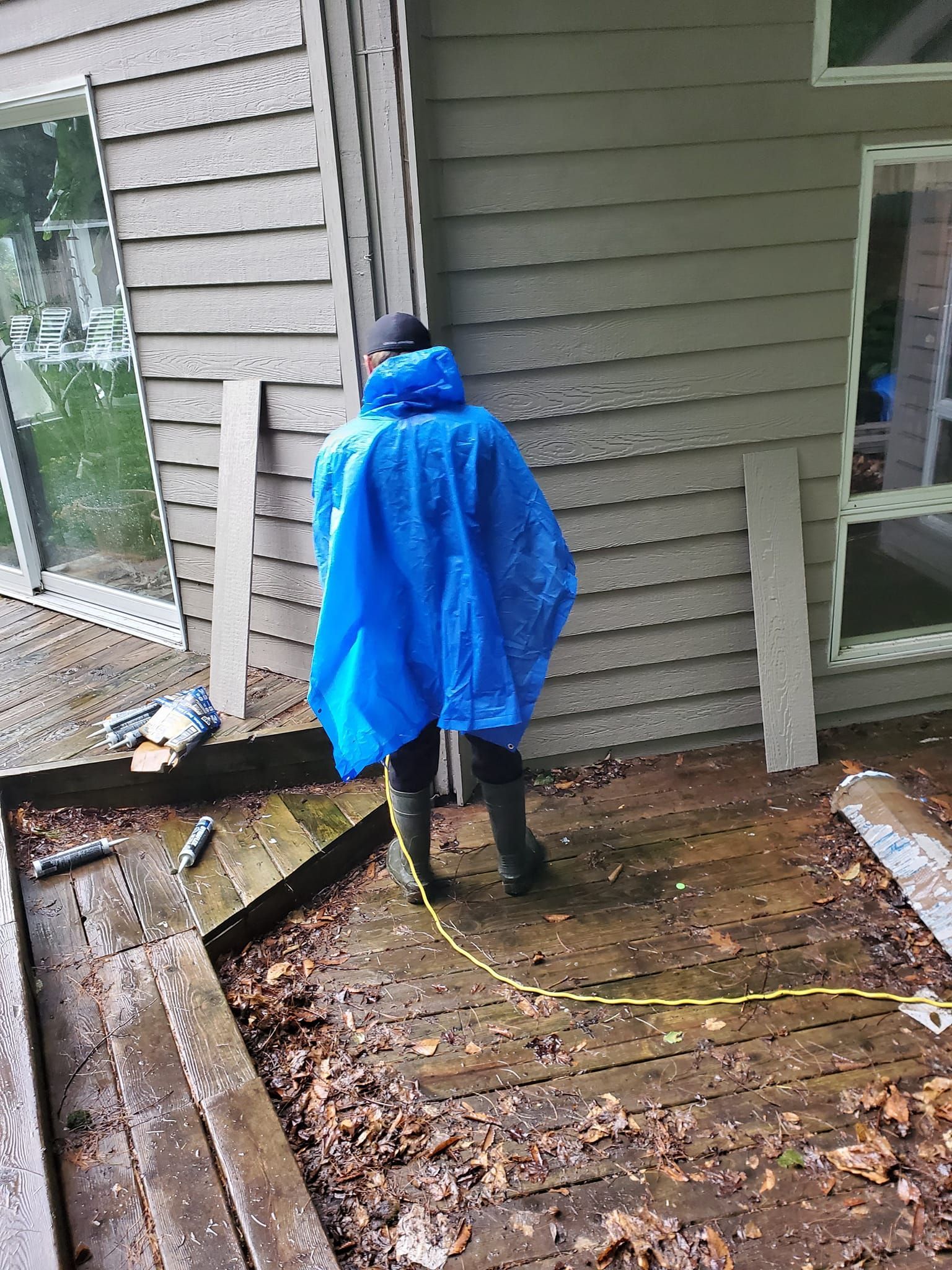 Person in blue rain poncho working beside a house on a wet, muddy porch