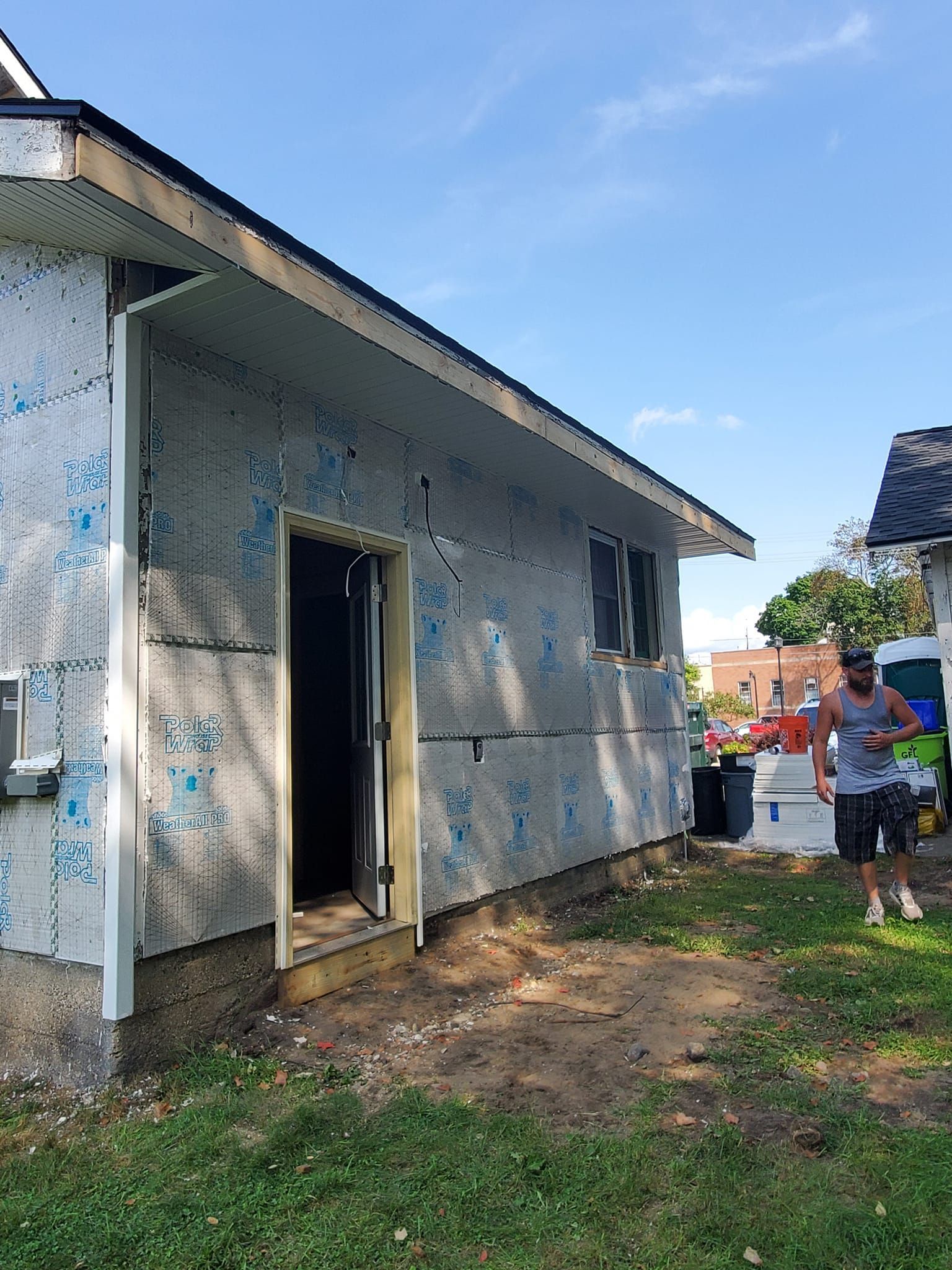 Partially constructed house exterior with open doorway; two people stand near the right side under a blue sky.